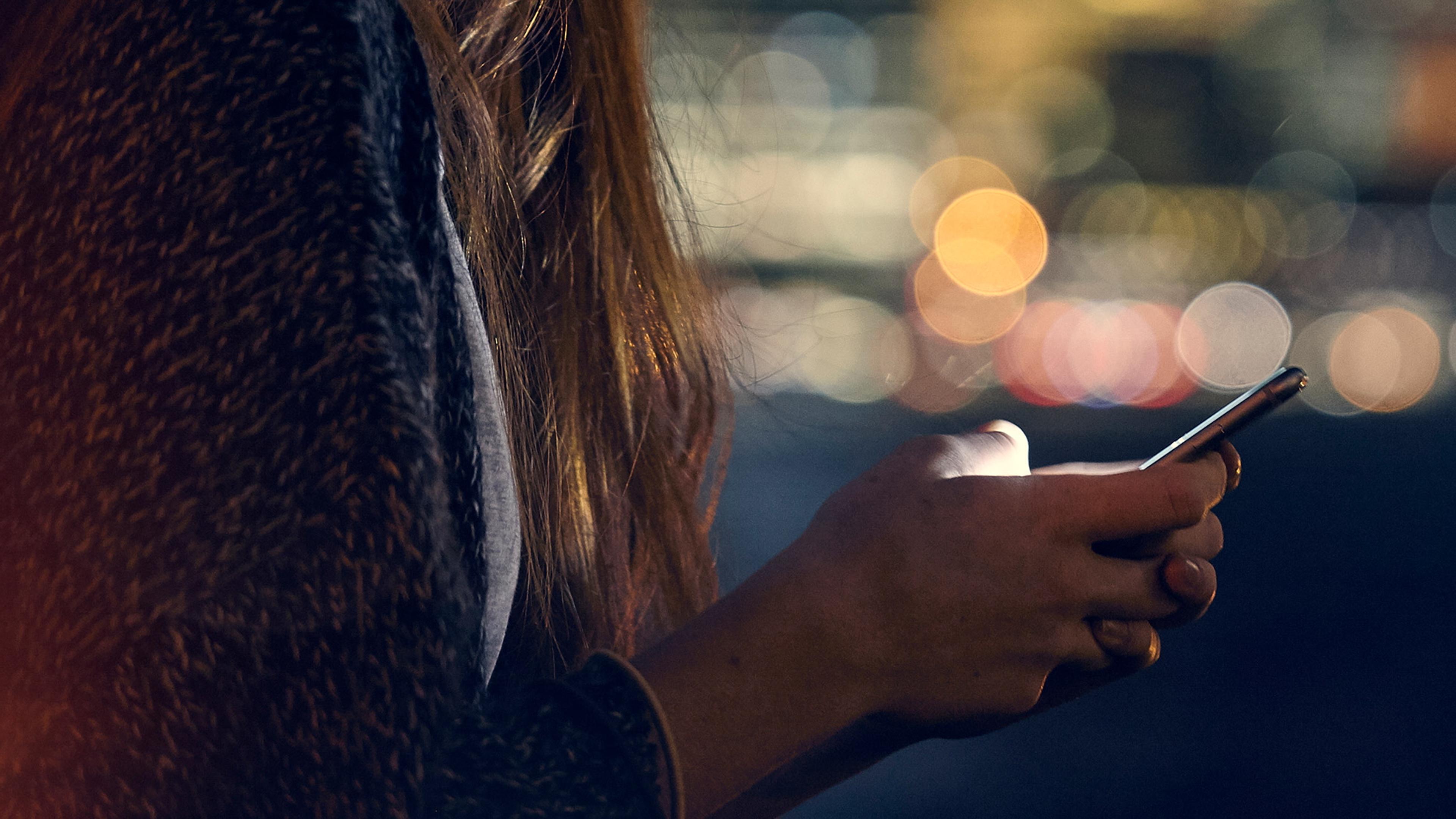 Close-up of a person’s hands using a smartphone at night, with blurred city lights in the background.