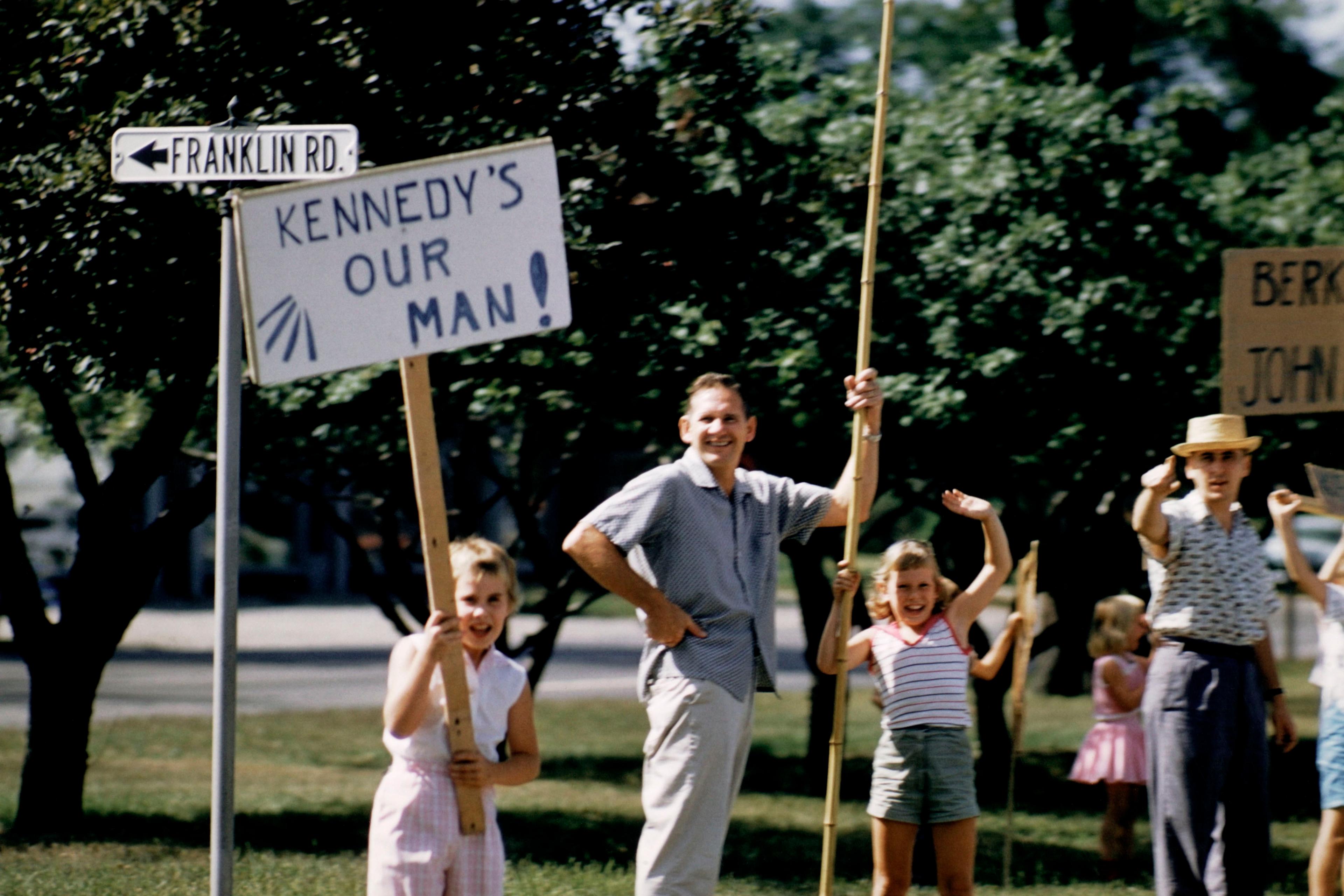 Photo of people holding signs supporting Kennedy on Franklin Rd surrounded by trees.