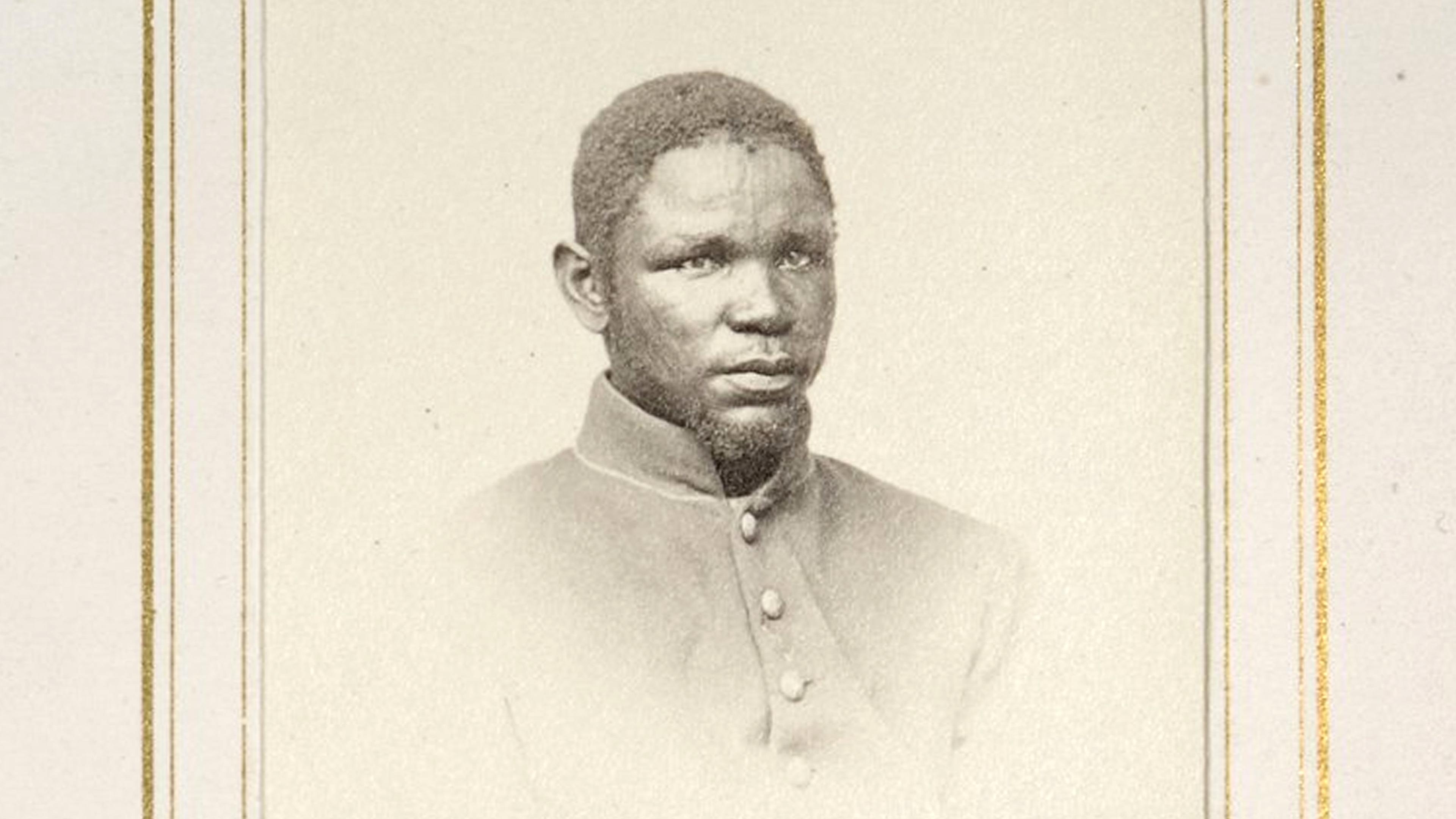 Vintage sepia photo of a Black man in a buttoned coat against a plain background with decorative border.