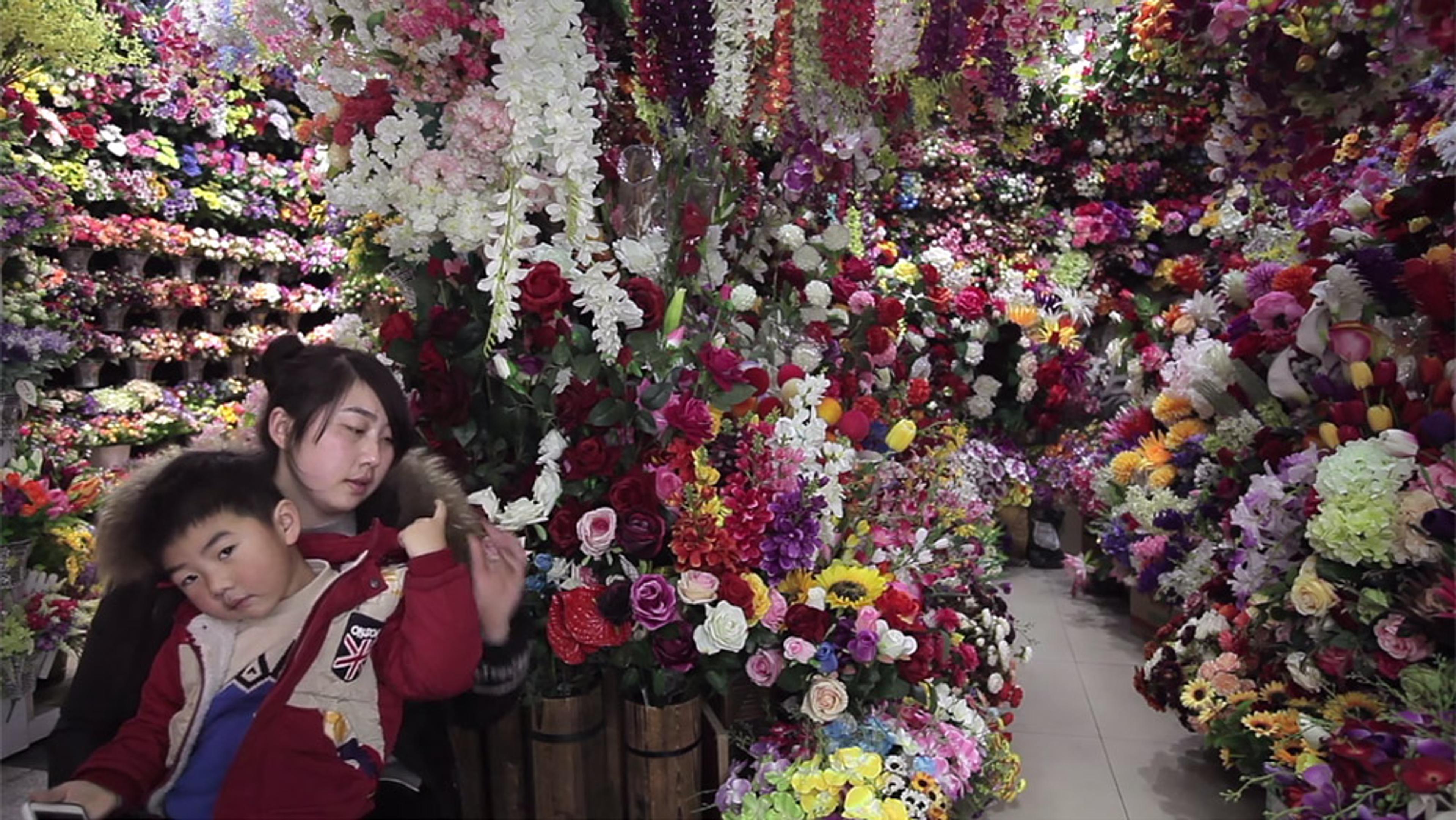 A woman and a boy surrounded by a vast array of colourful flowers in what appears to be a flower shop or market.
