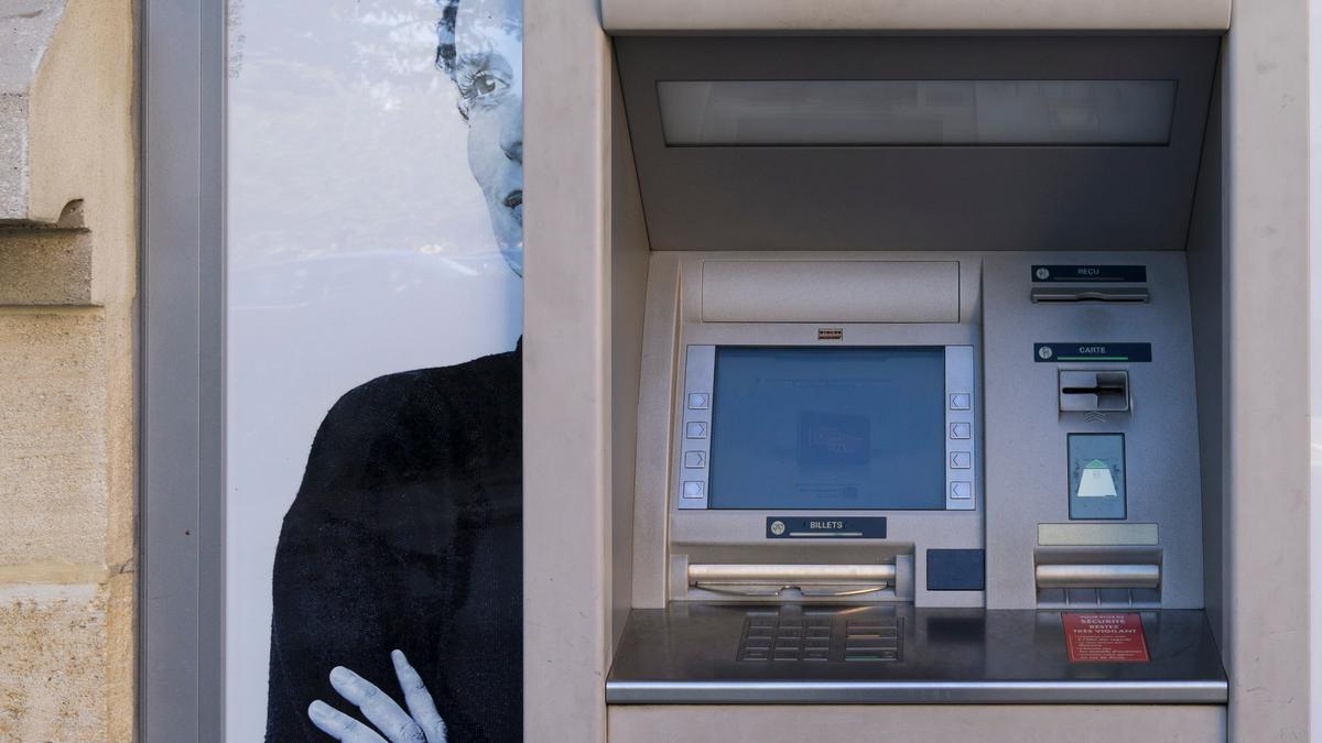 An ATM in front of a poster of a woman with arms crossed.