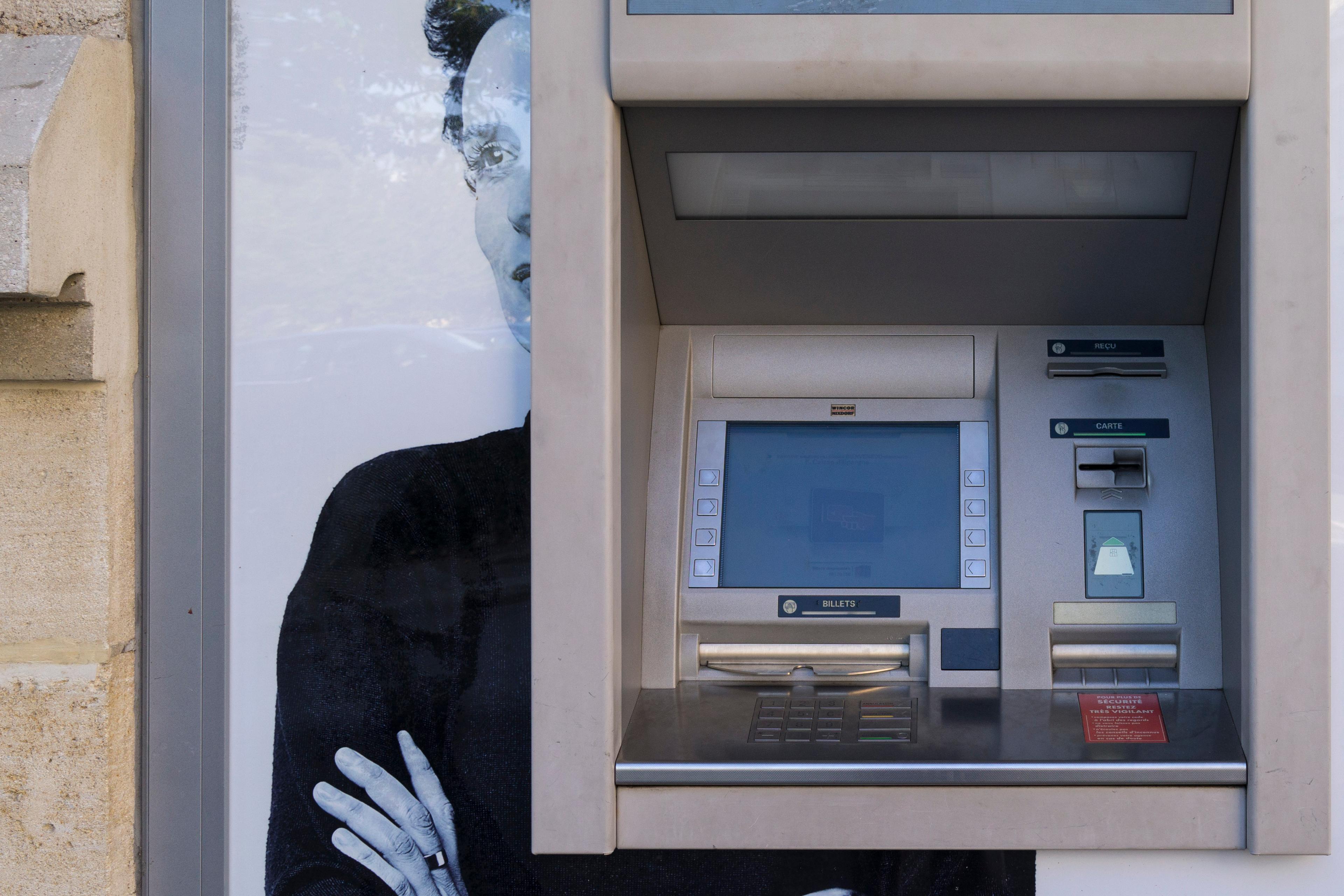An ATM in front of a poster of a woman with arms crossed.