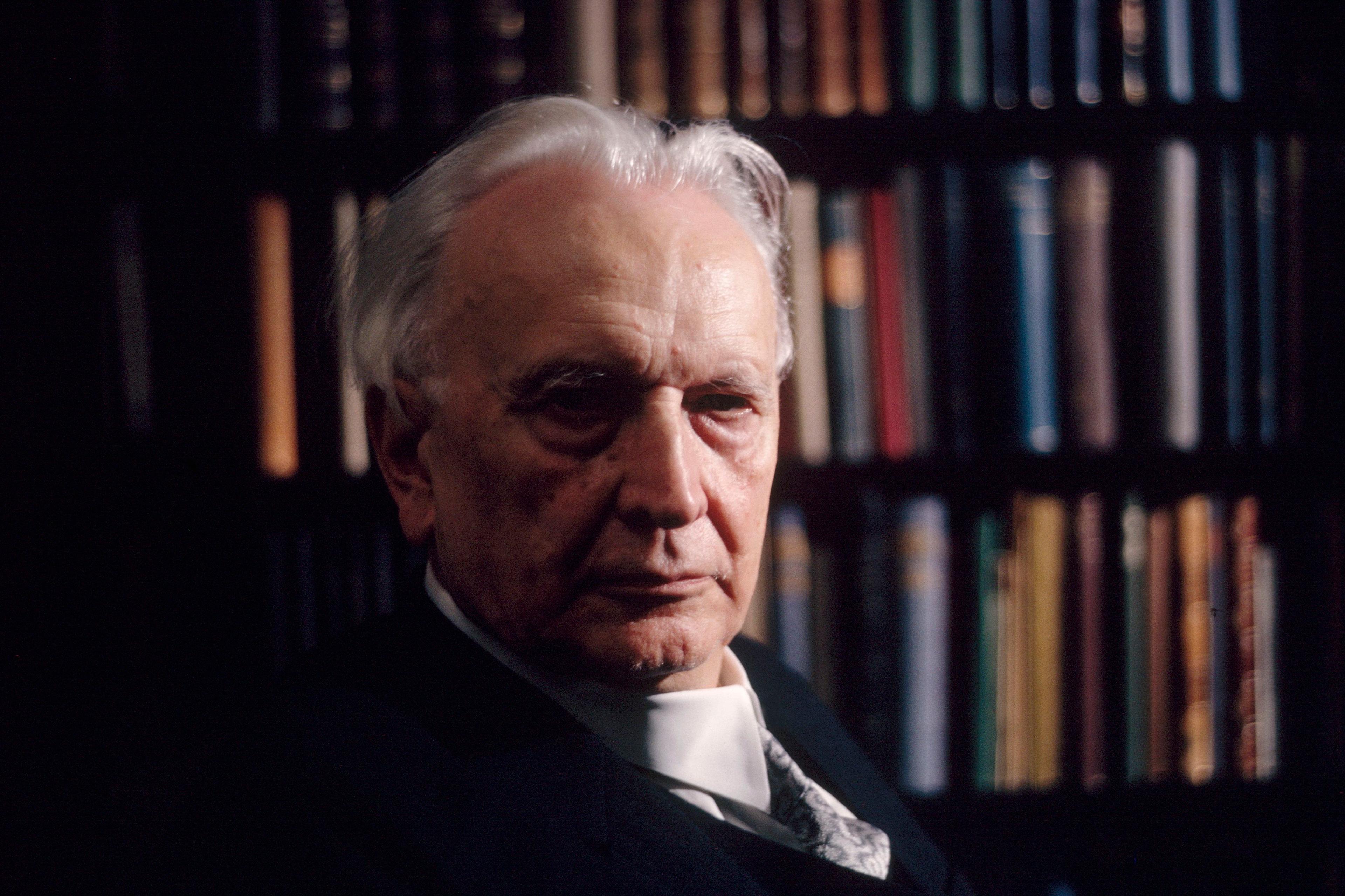 Photo of an elderly man with grey hair in front of a bookshelf filled with colourful books.