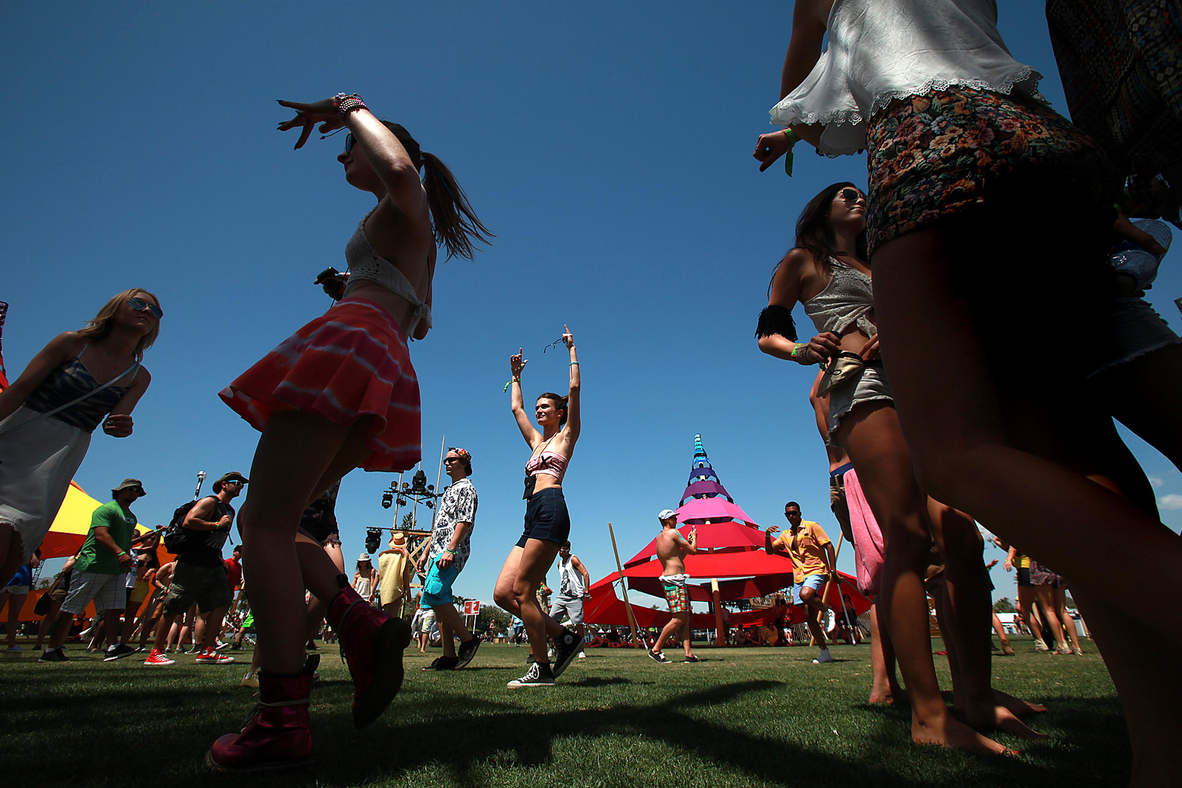 People dancing at an outdoor festival, colourful tents in background, clear blue sky overhead.