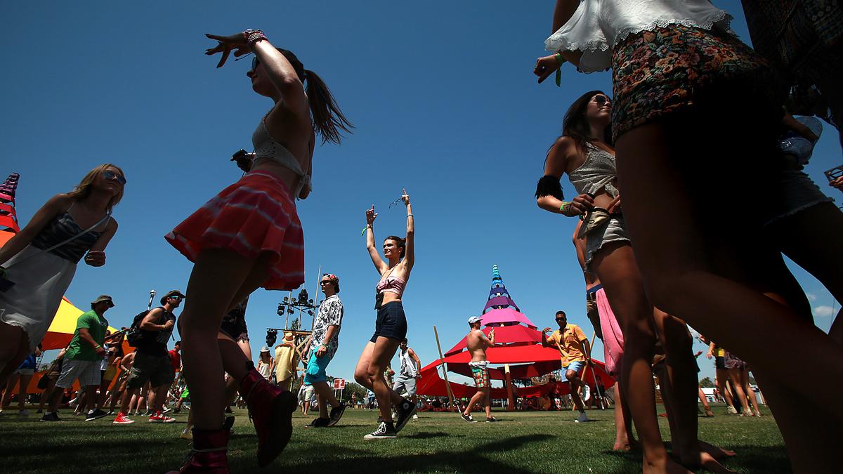 People dancing at an outdoor festival, colourful tents in background, clear blue sky overhead.