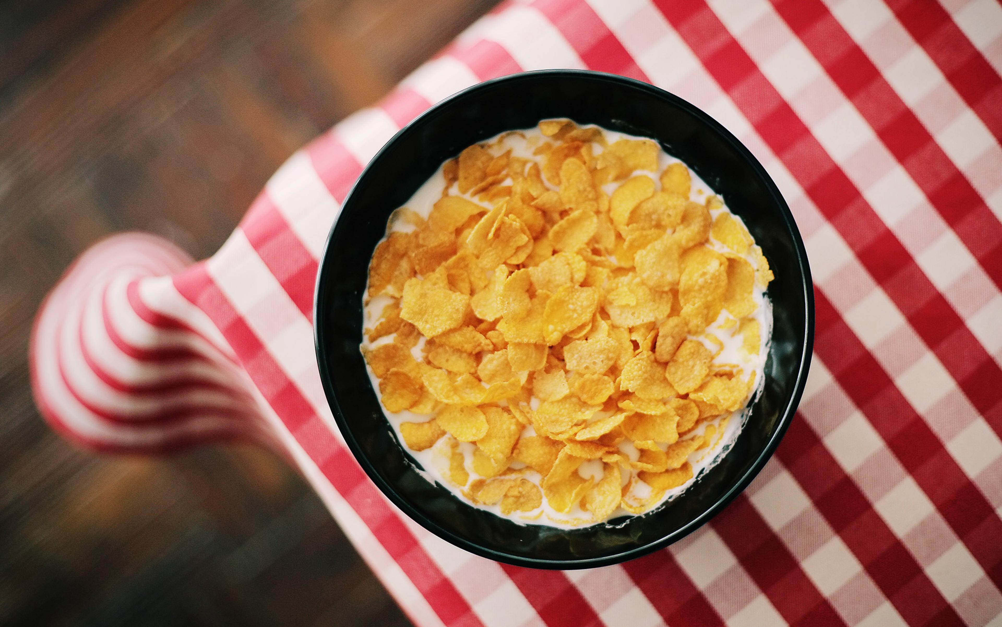A bowl of cornflakes and milk on a red and white checkered tablecloth.