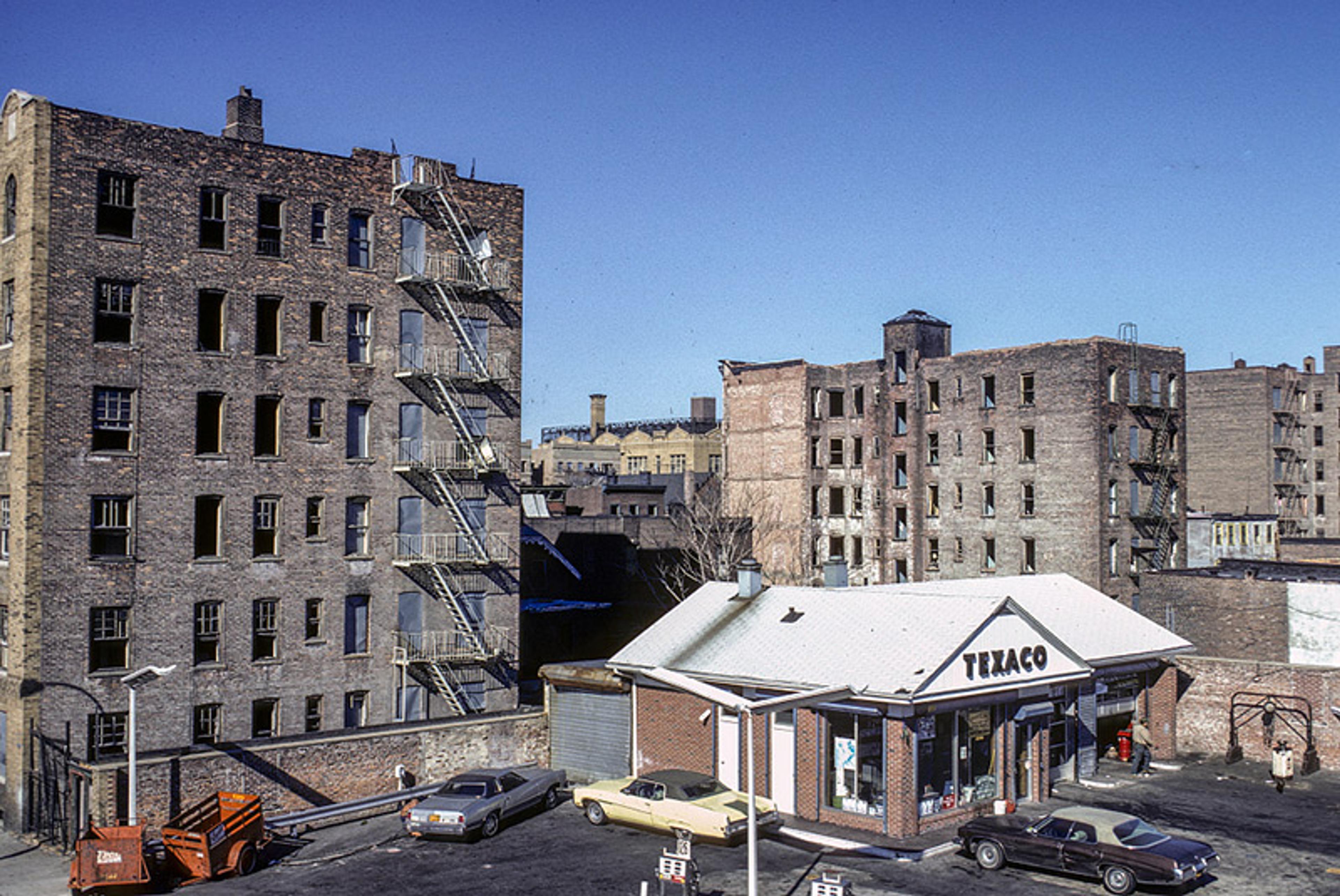 A Texaco gas station is depicted against a backdrop of abandoned apartment buildings