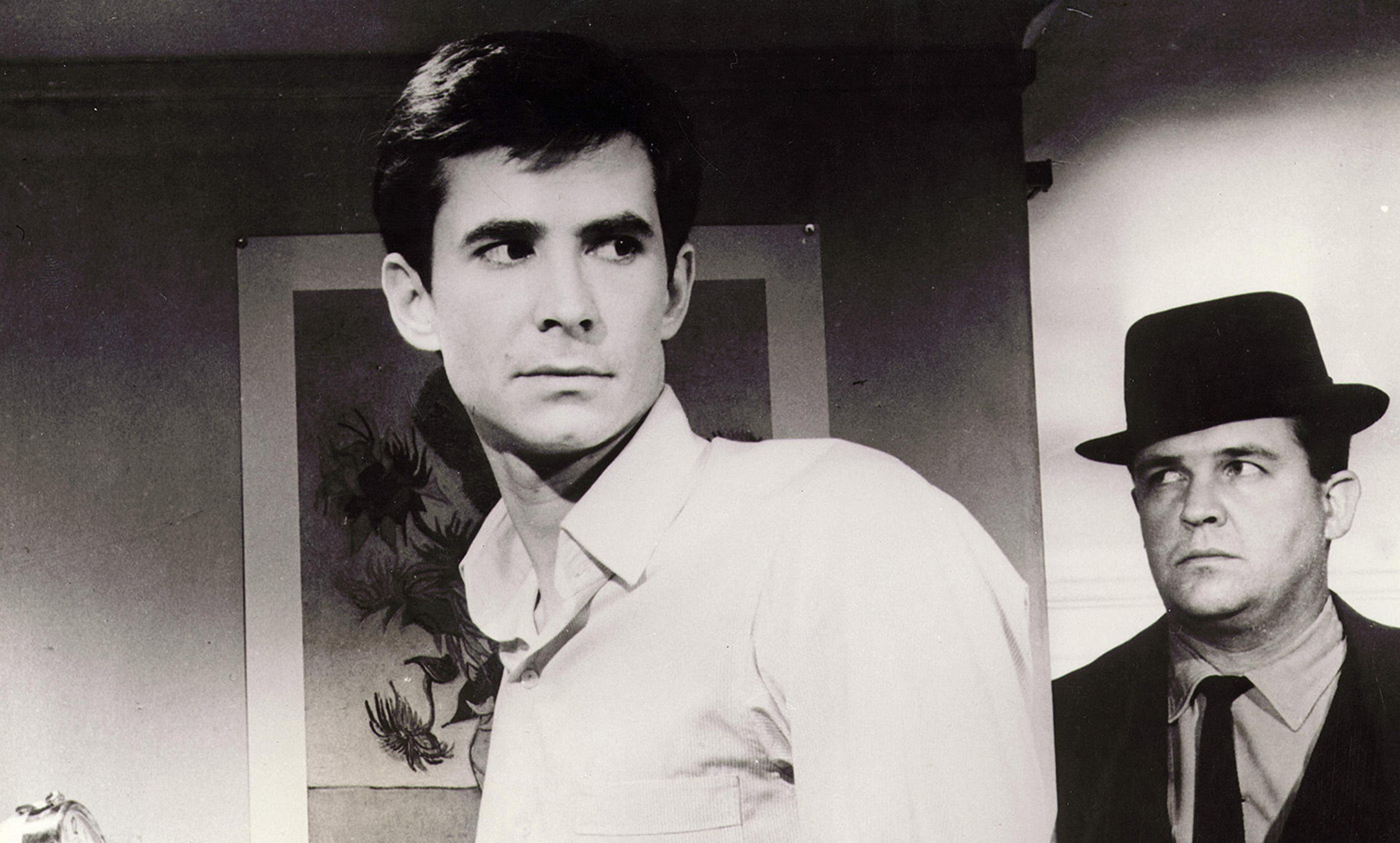 Black-and-white photo of two men, one in a white shirt and the other in a suit with a hat, in a room with artwork on the wall.