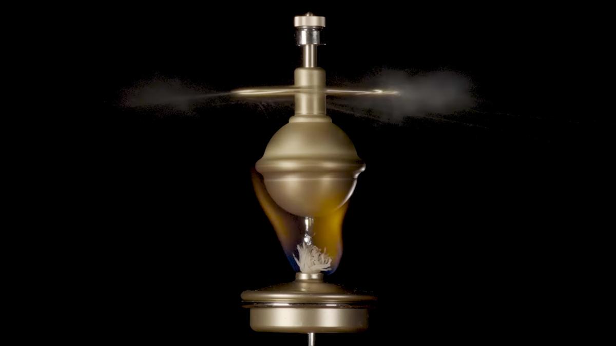 Photo of a brass steam engine toy in motion with steam jets visible against a black background.