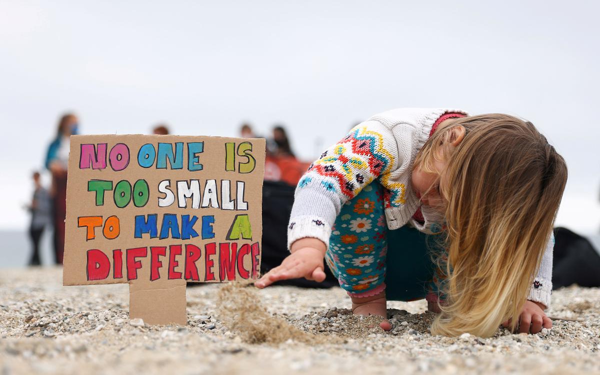 A young child on a beach beside a sign that reads “No one is too small to make a difference” in colourful letters.