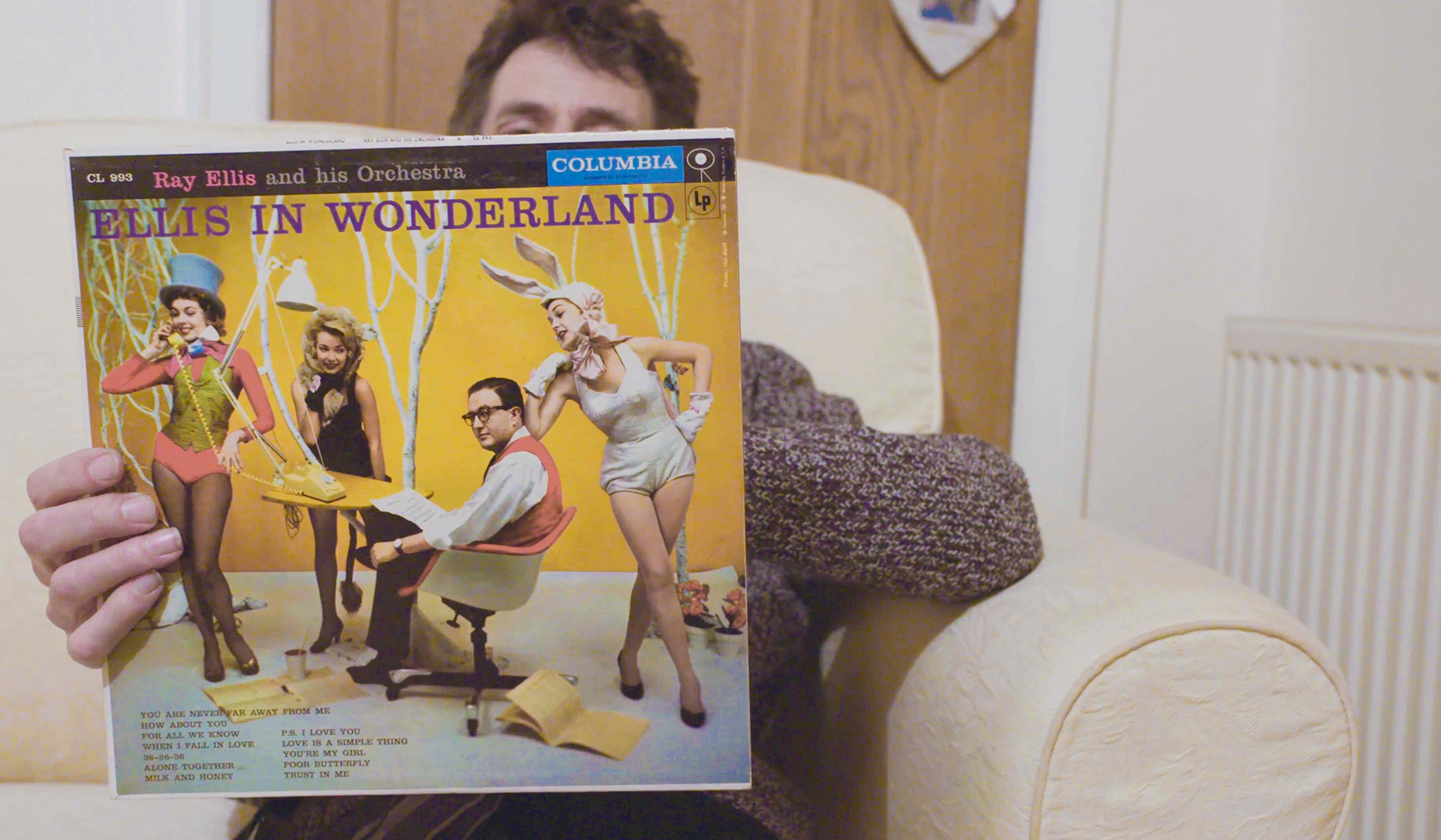 Person holding the “Ellis in Wonderland” album cover by Ray Ellis and his Orchestra, featuring a colourful, whimsical scene.
