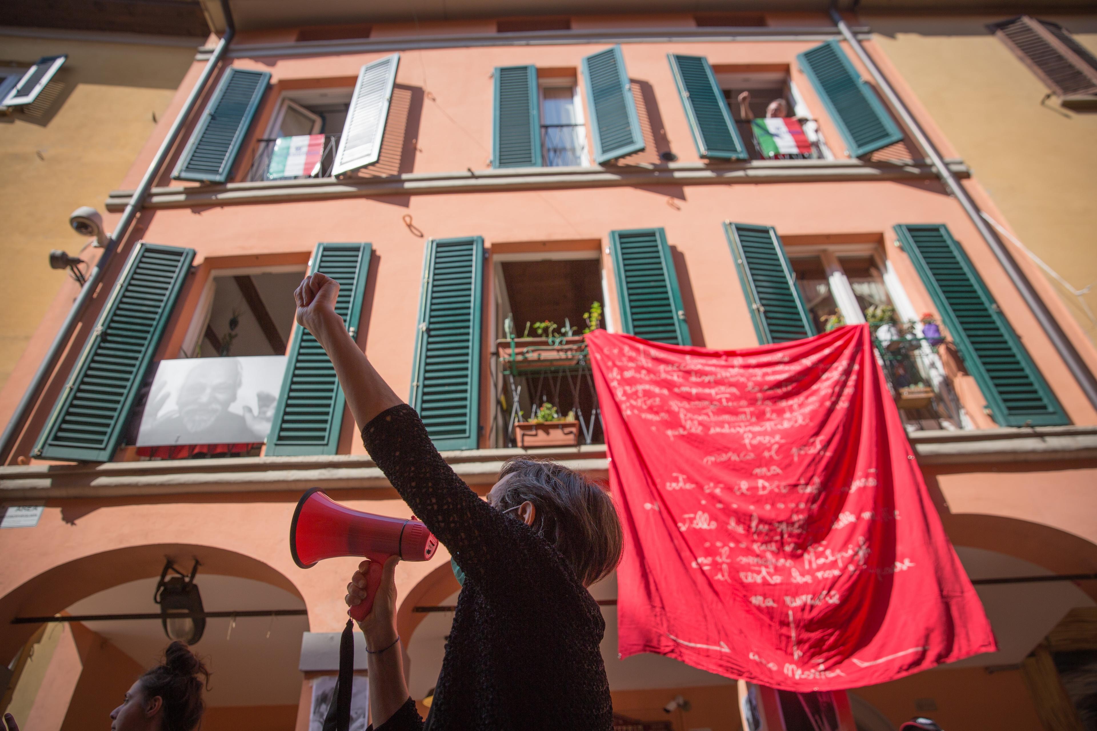 Photo of a person with a megaphone raising a fist below a building with green shutters and a red banner.