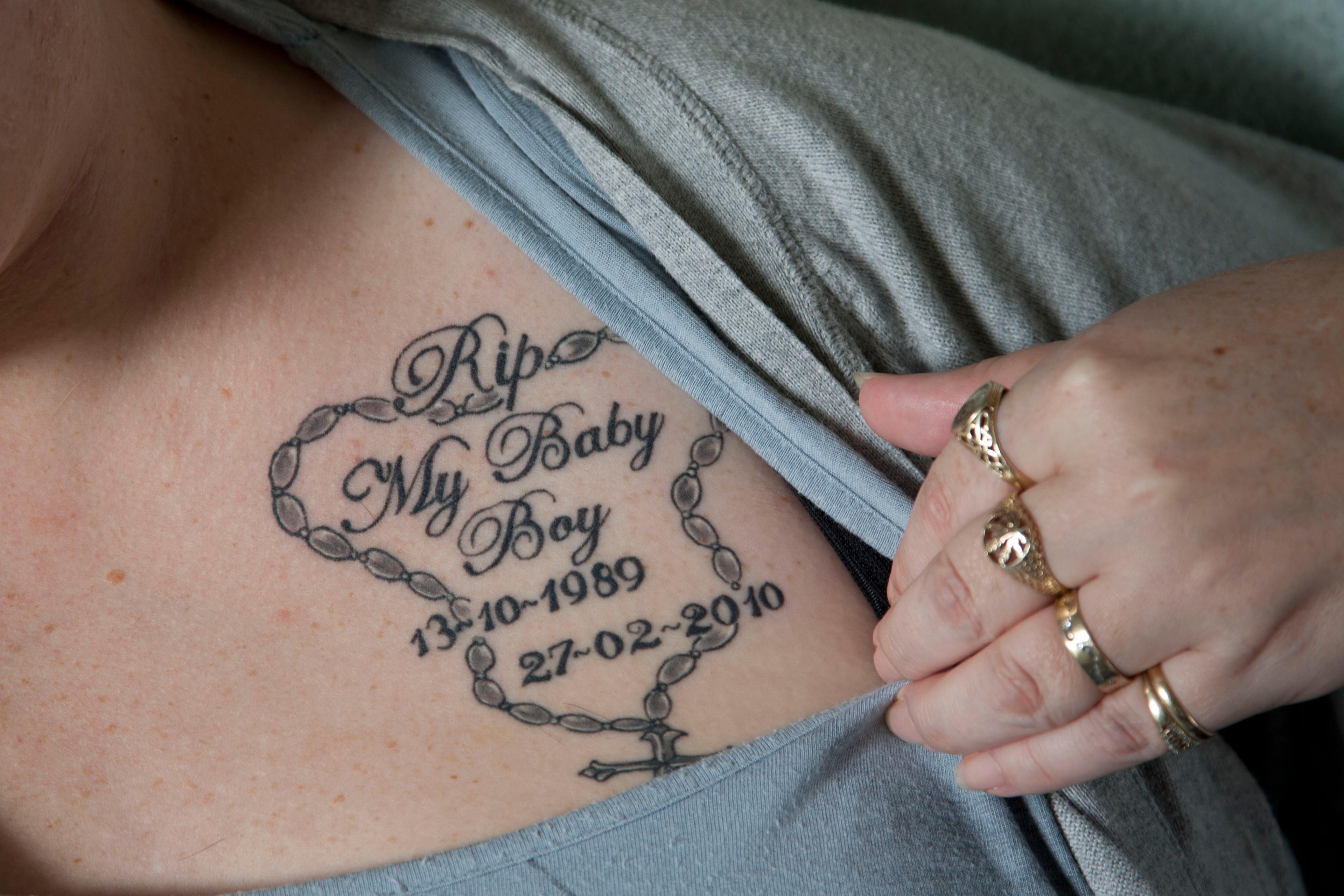 Photo of a tattoo on a person’s chest. It reads “RIP My Baby Boy” with dates and a rosary design around the text.