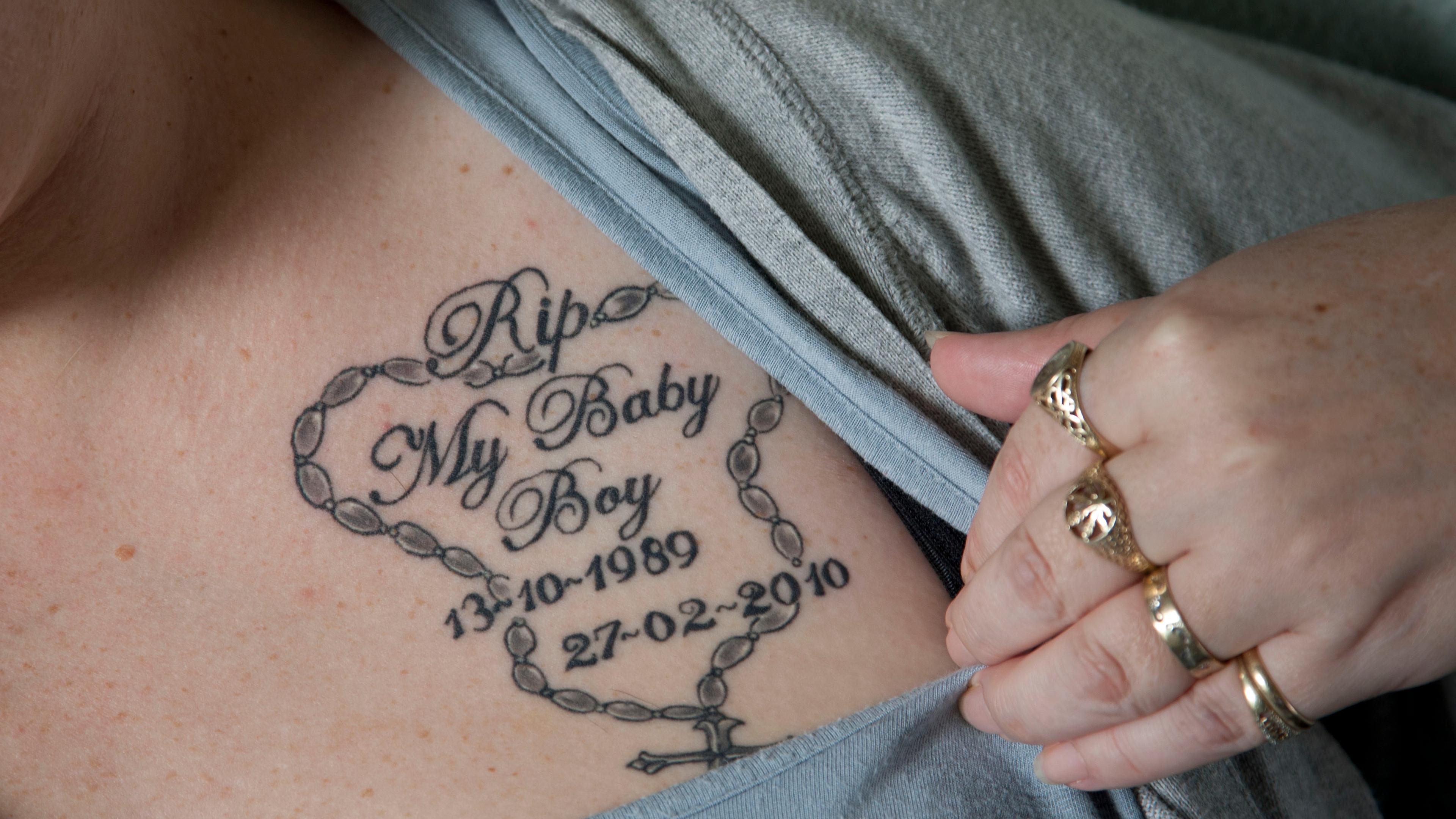 Photo of a tattoo on a person’s chest. It reads “RIP My Baby Boy” with dates and a rosary design around the text.