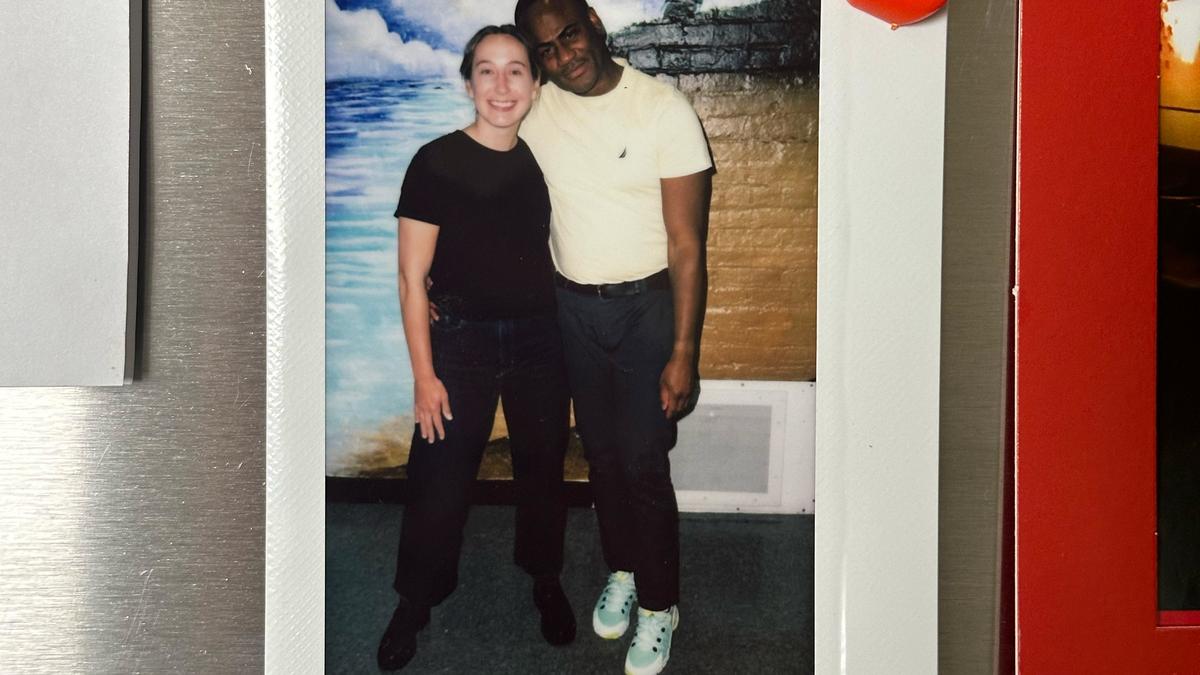 A Polaroid photo of two people standing together smiling in front of a painted mural depicting the sea and clouds.