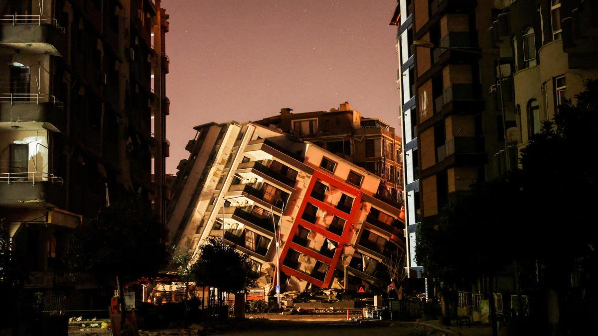 A collapsed apartment building leaning between other damaged buildings in twilight