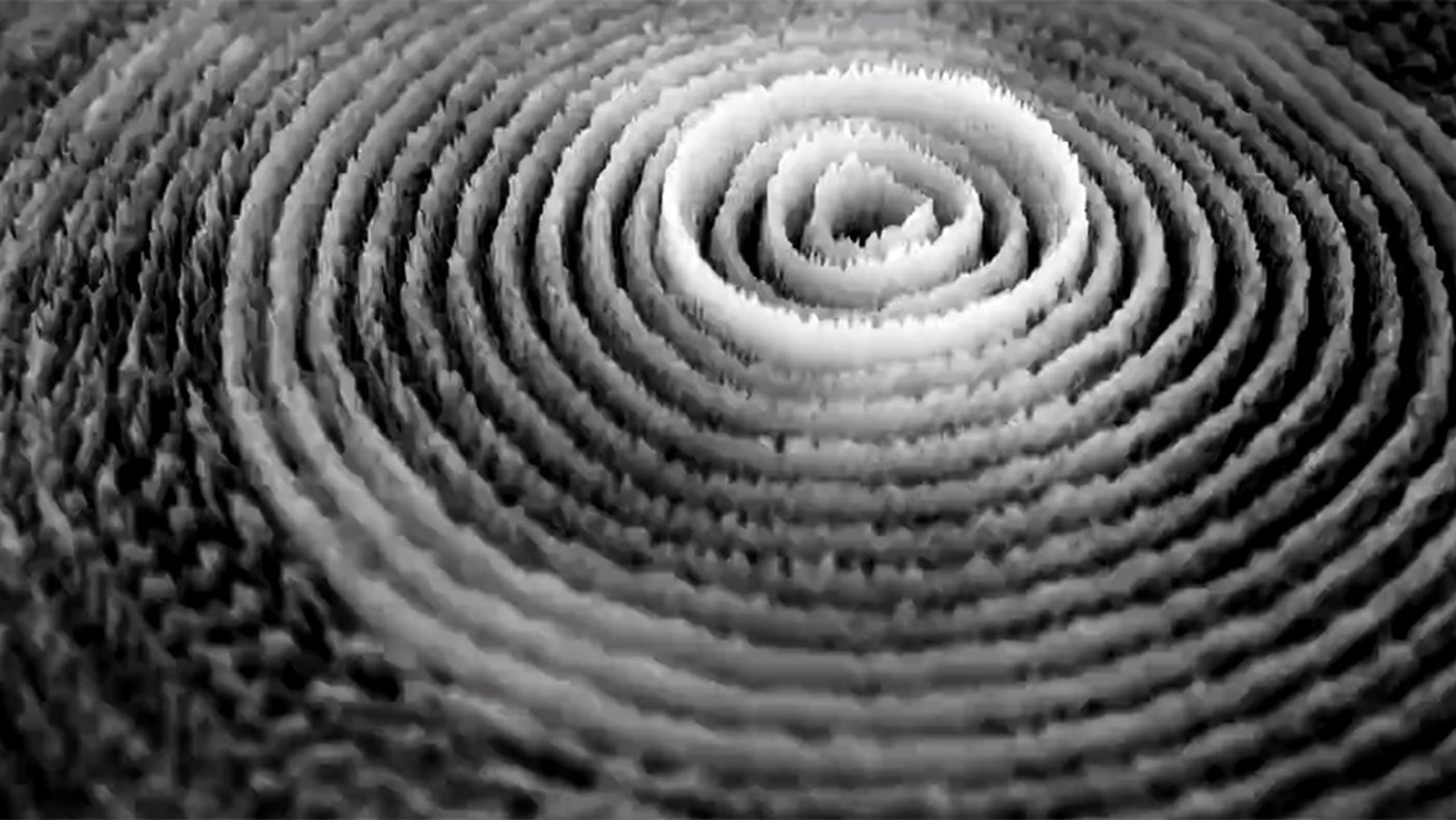 Monochrome photo of concentric circular patterns resembling sound waves or ripples viewed from above forming a deep central hole.
