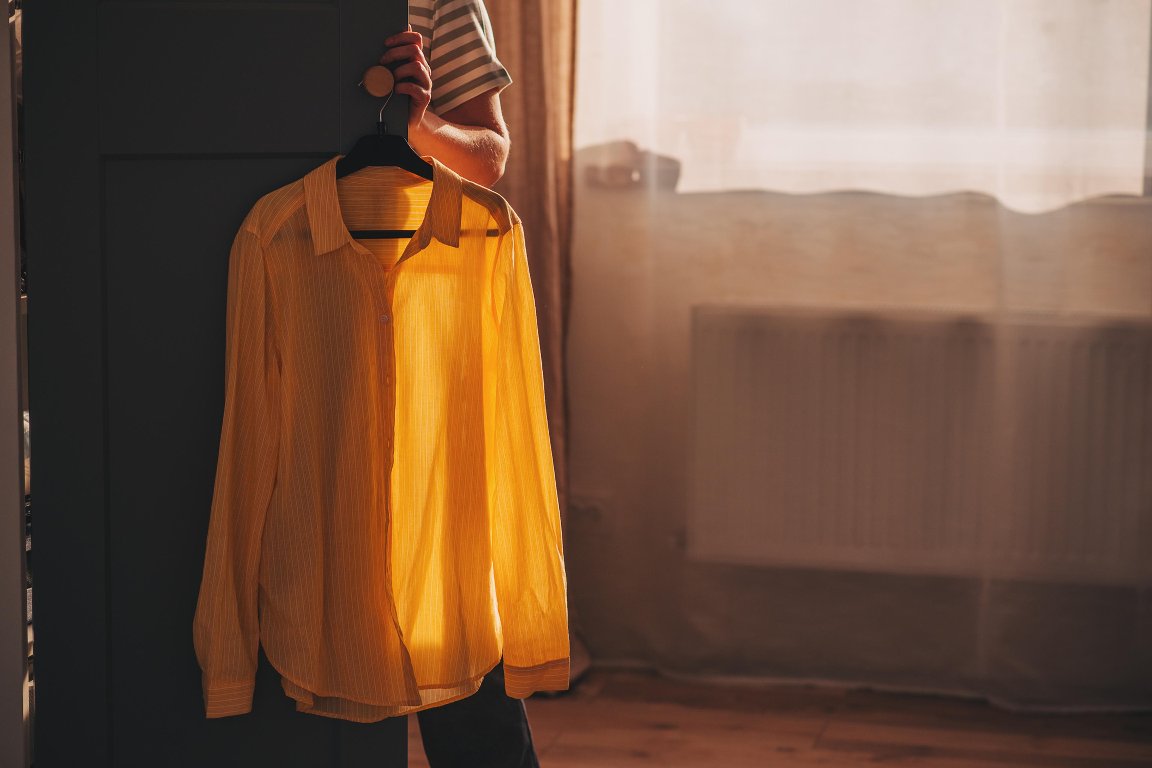 A yellow shirt on a hanger by a door with sunlight streaming in through a window in the background.
