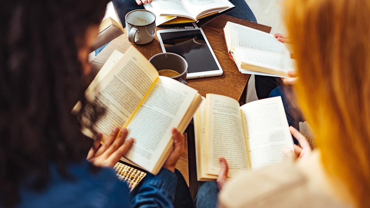 People sitting around a table reading books with a tablet and mugs visible.