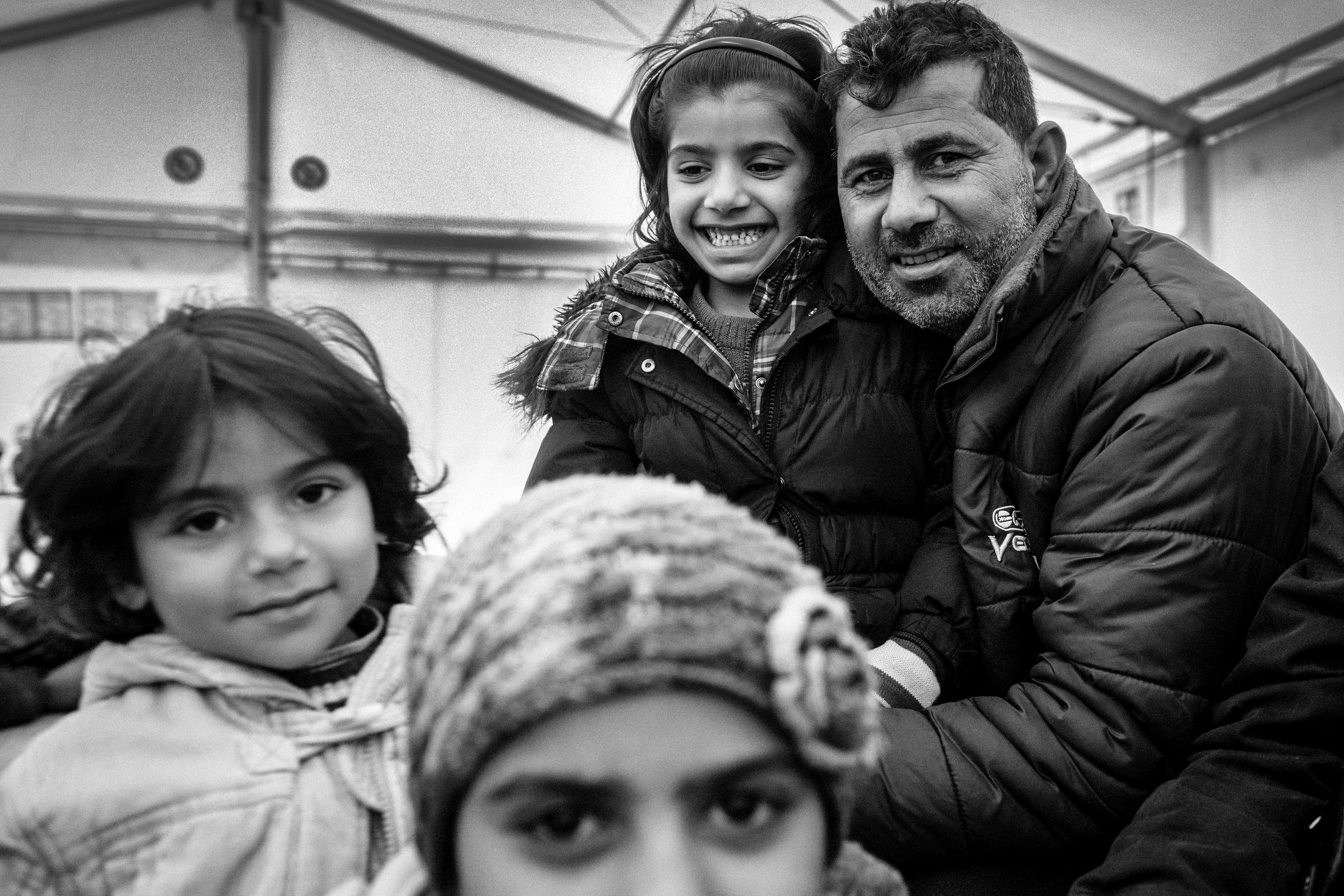 Black and white photo of a smiling man with three children in warm clothing indoors.