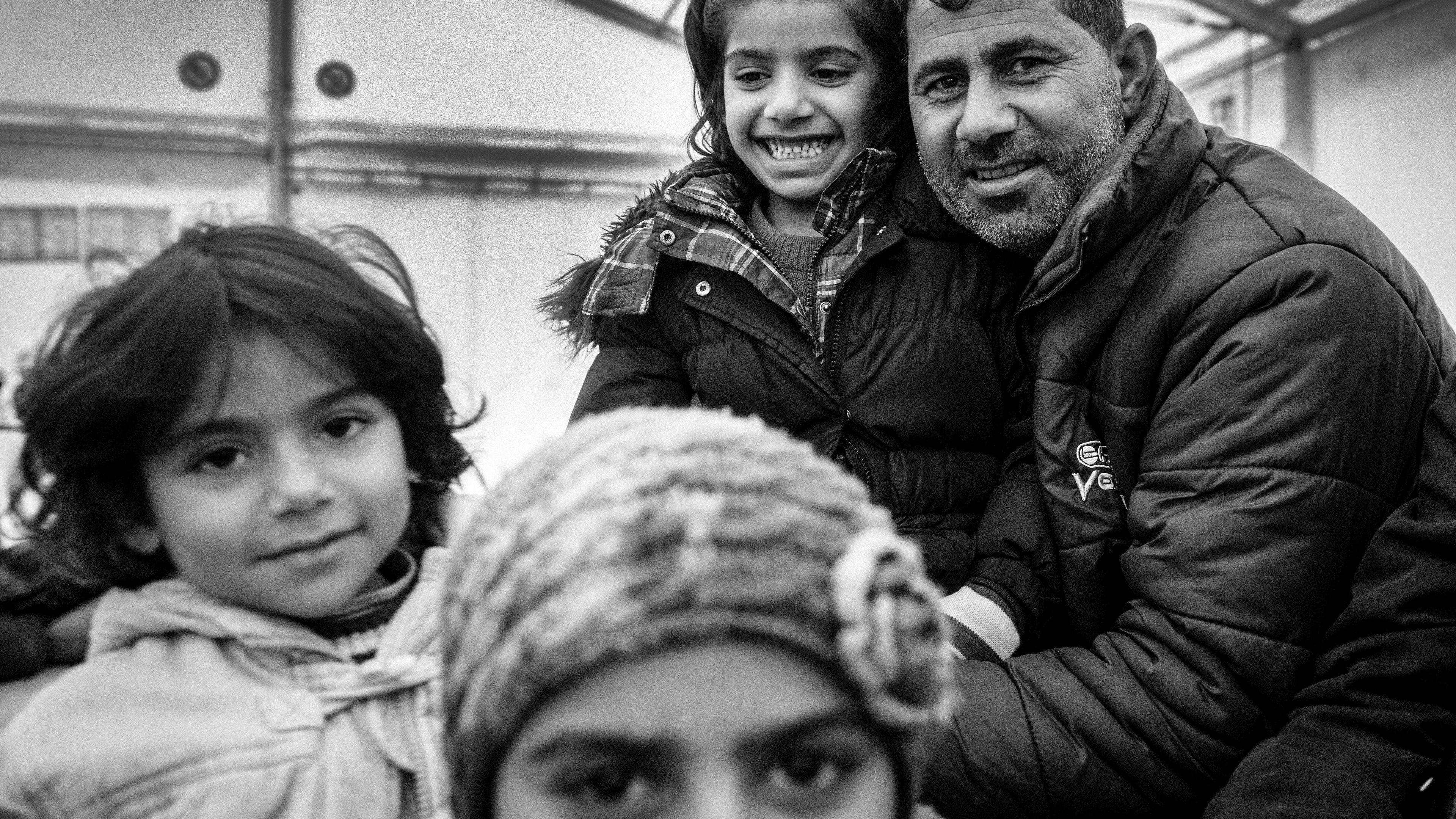 Black and white photo of a smiling man with three children in warm clothing indoors.
