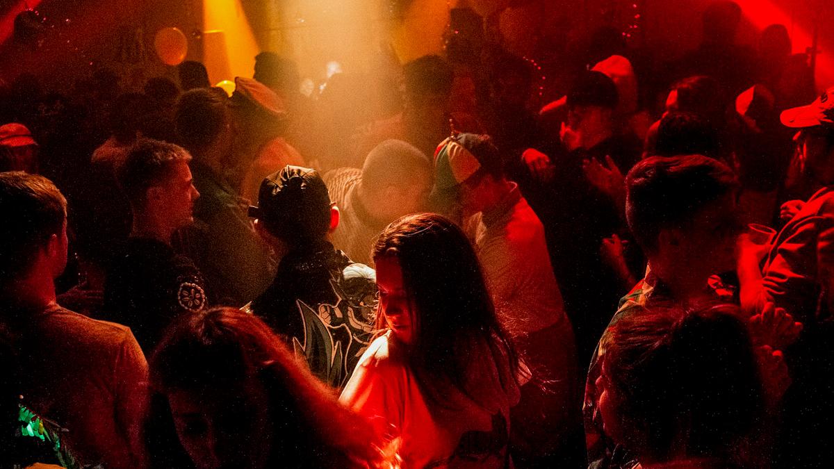 Photo of a crowded nightclub with people dancing under red and orange lights, creating a lively atmosphere.