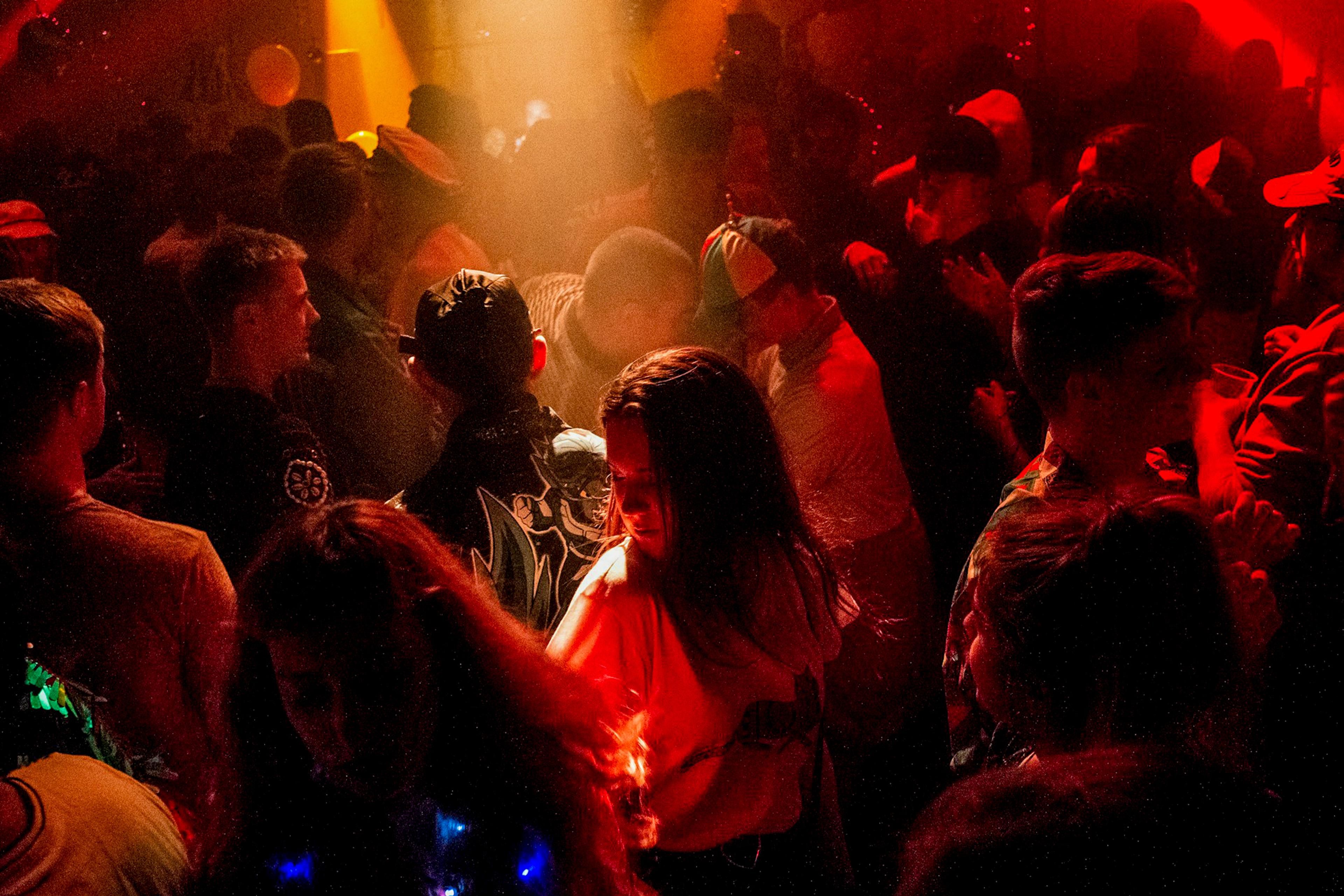 Photo of a crowded nightclub with people dancing under red and orange lights, creating a lively atmosphere.