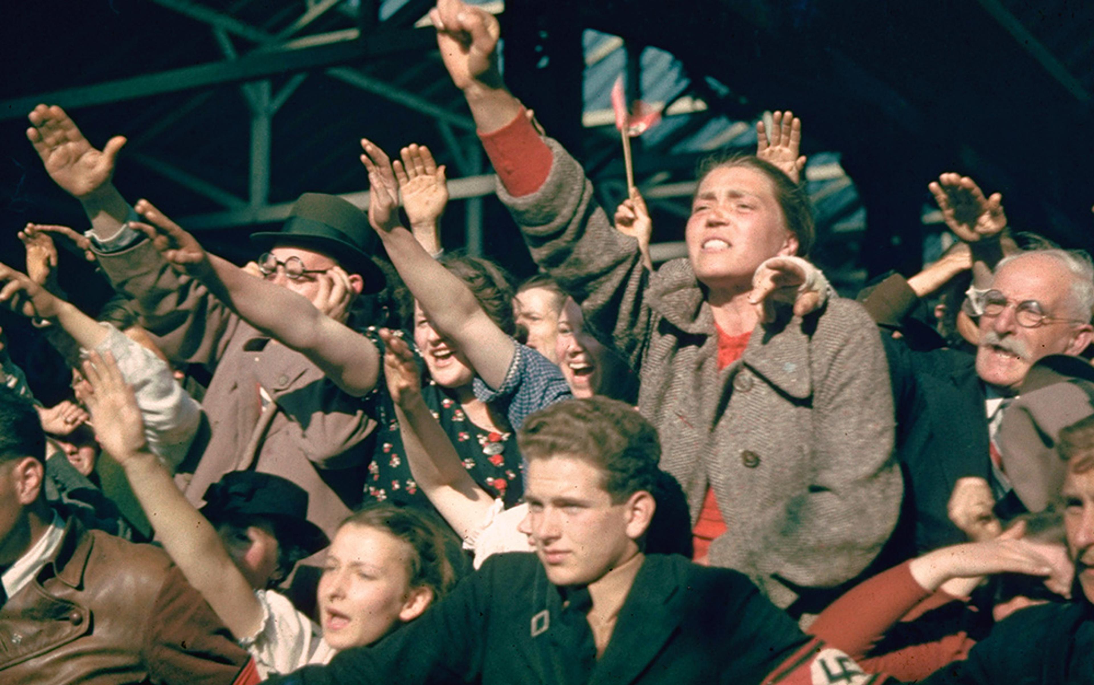 Vintage photo of an enthusiastic crowd raising their arms in a salute, some wearing swastikas.