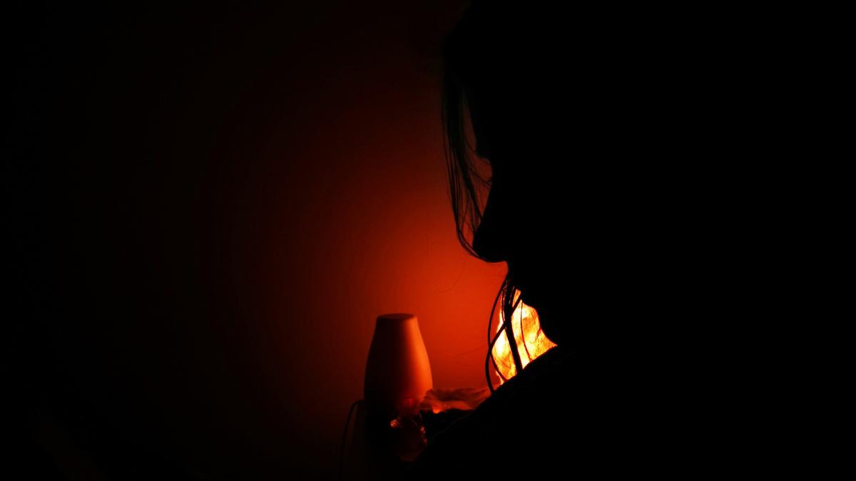 Silhouette of a person next to a glowing orange lamp in a dark room.