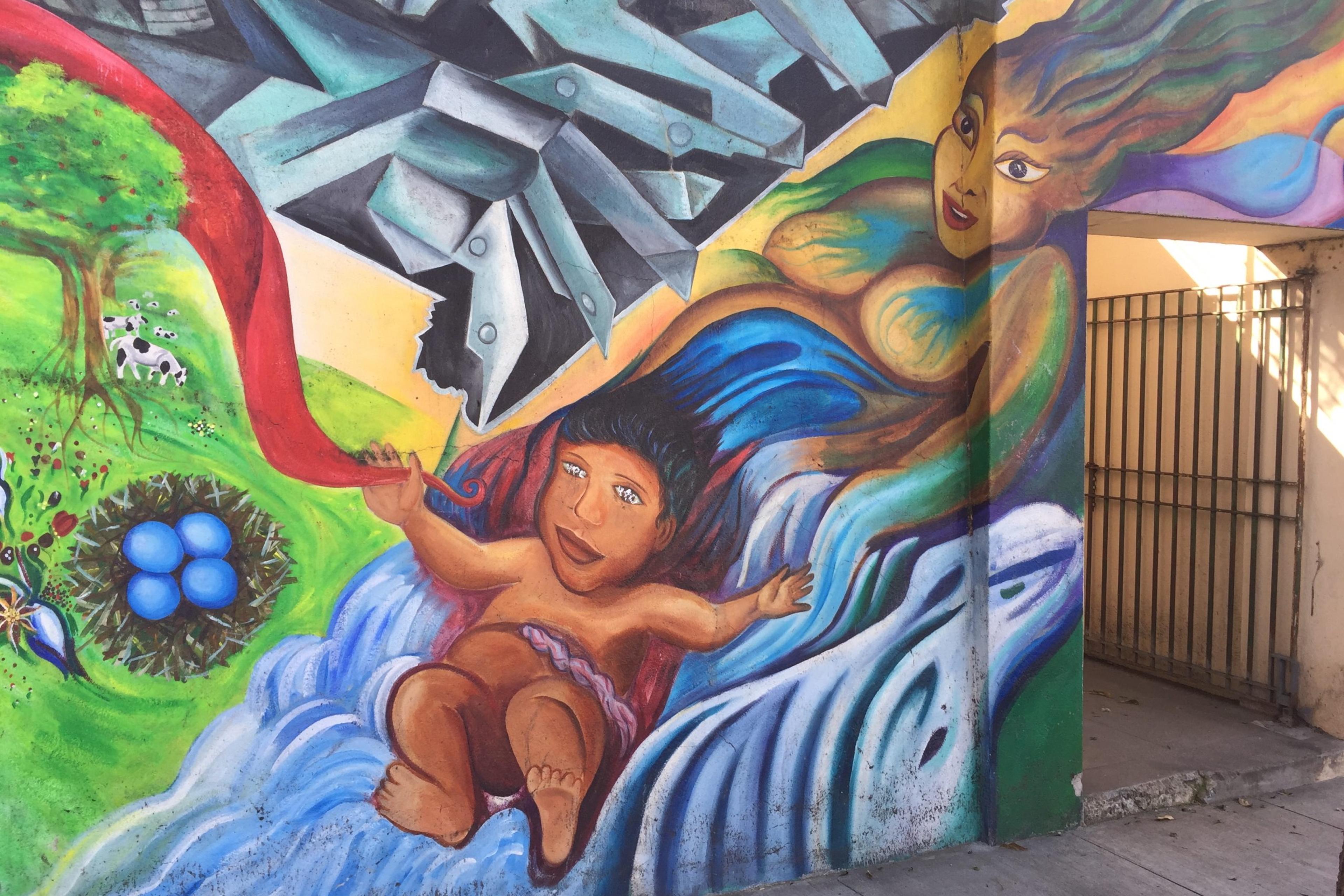 Colourful mural with a baby floating on water, a woman, a tree, and birds’ eggs. Abstract shapes fill the background.