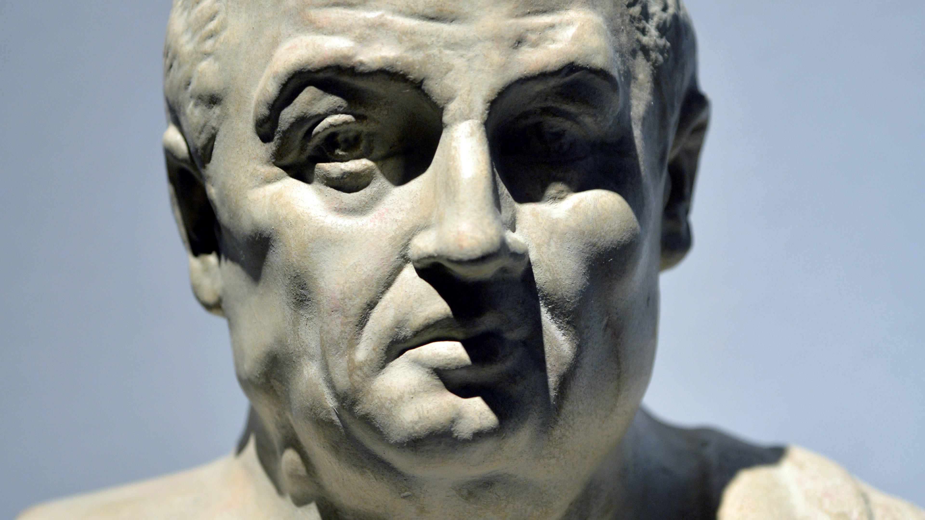 Bust of a man in marble against a plain background, showcasing detailed facial features and draped garment; sculpture.