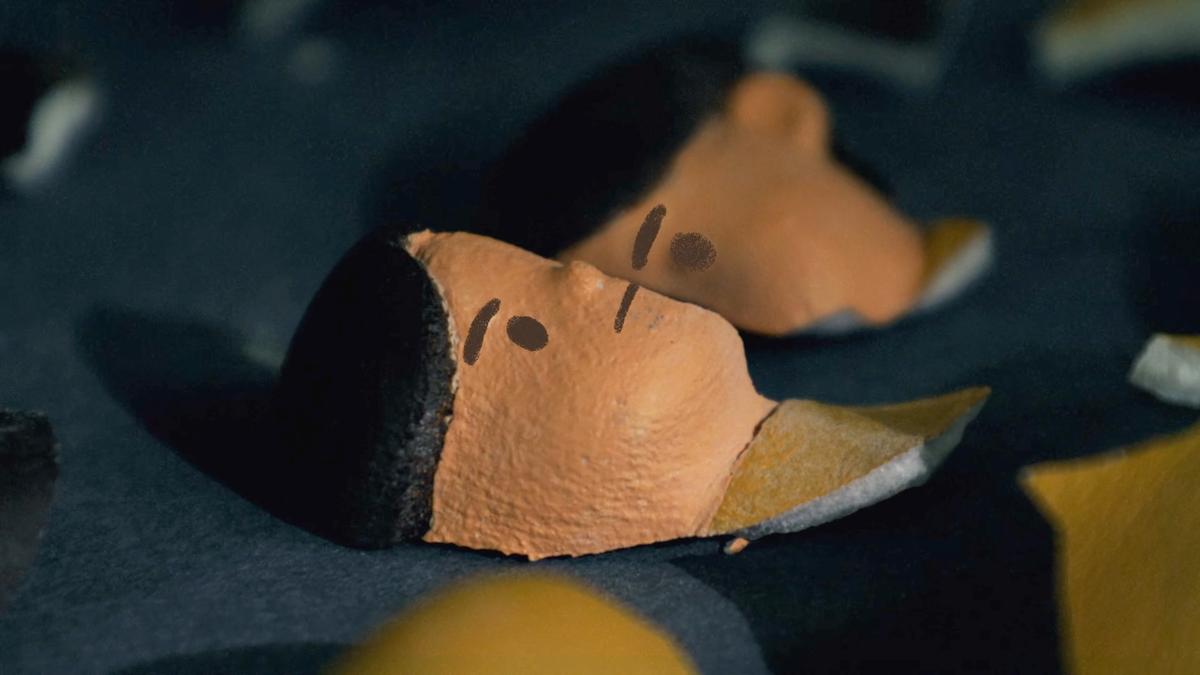 Two clay faces with minimal features lying on a dark surface in a close-up photograph.