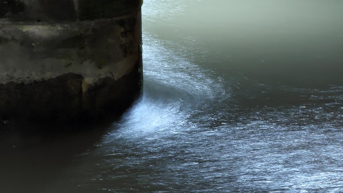 Water swirling around a concrete structure in low light, creating a reflective and slightly turbulent surface.