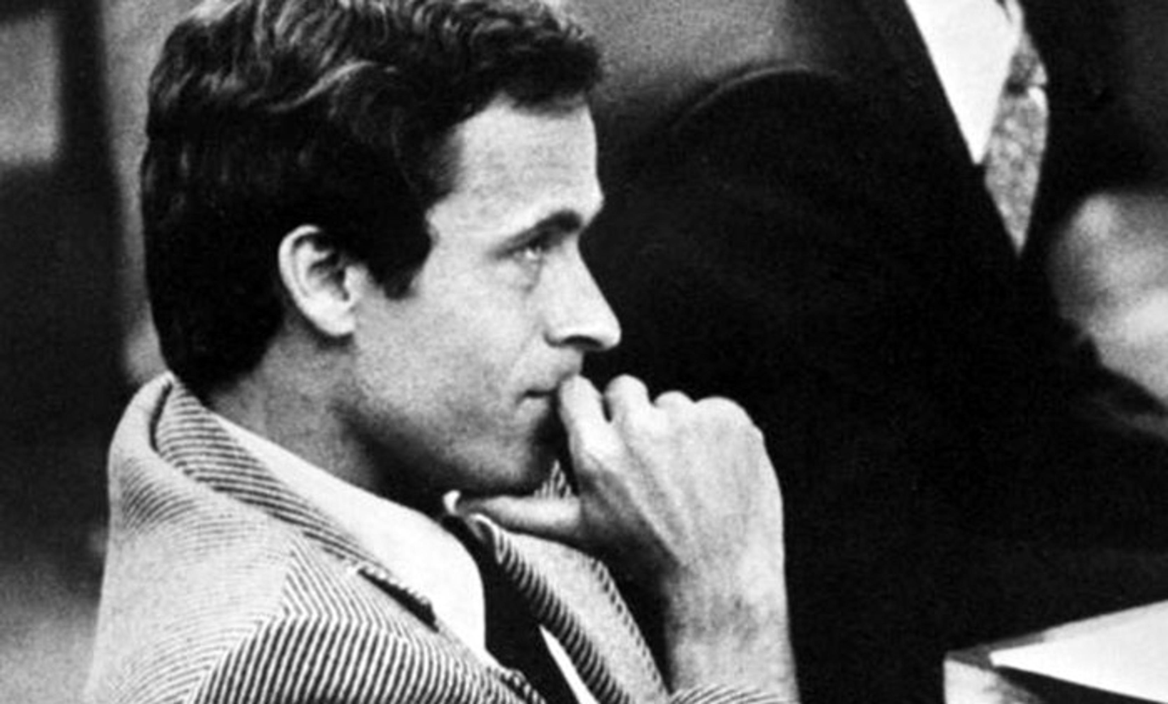 Black and white photo of a man in a suit, sitting with his hand on his chin, looking thoughtful during a formal event.
