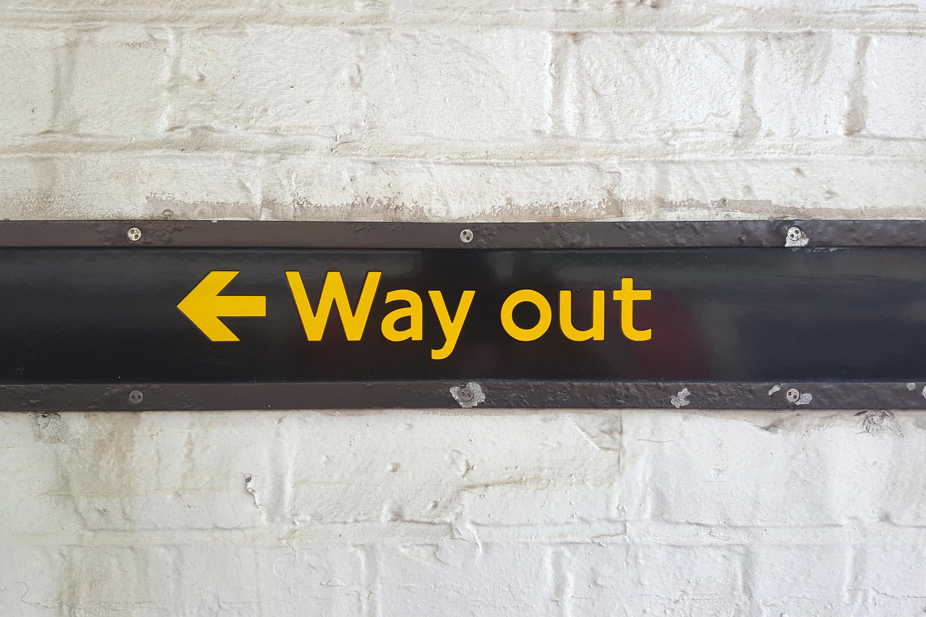 A sign on a brick wall reading “Way out” with a left arrow in yellow text on black background.