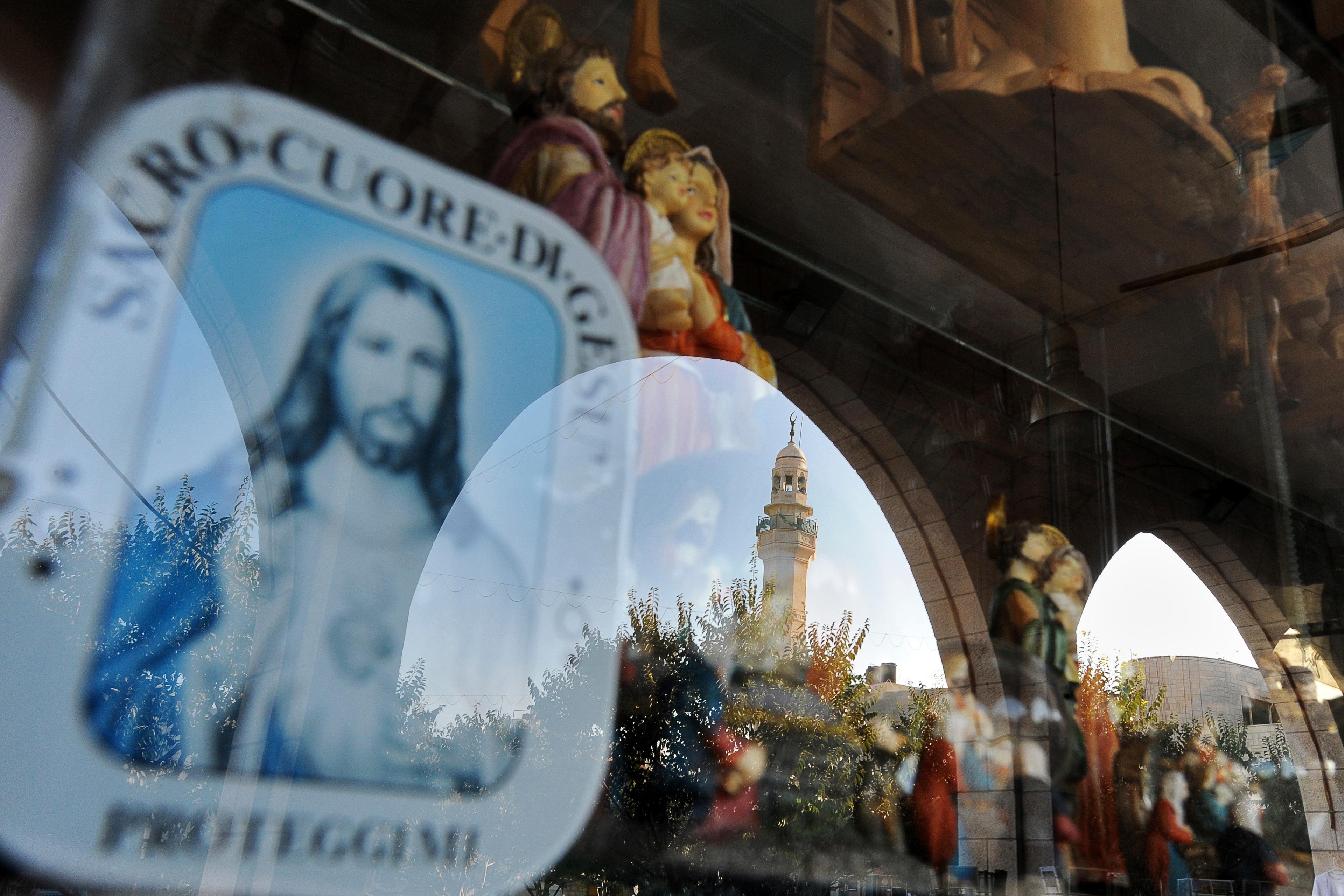 Photo of religious statues in a shop window with a reflection of an arch and a mosque tower in the background.