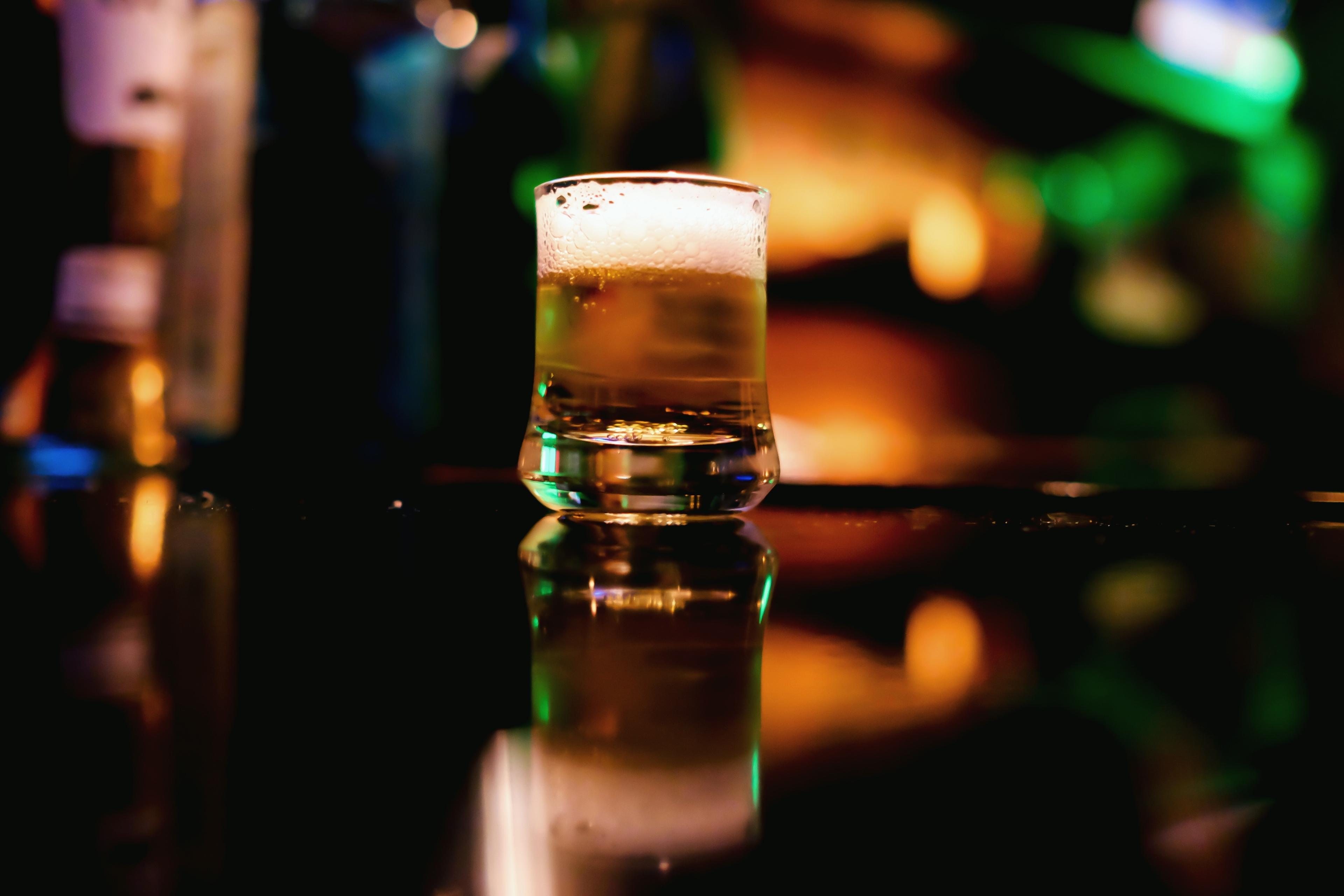 Photo of a glass of beer on a reflective surface with blurred colourful lights in the background.