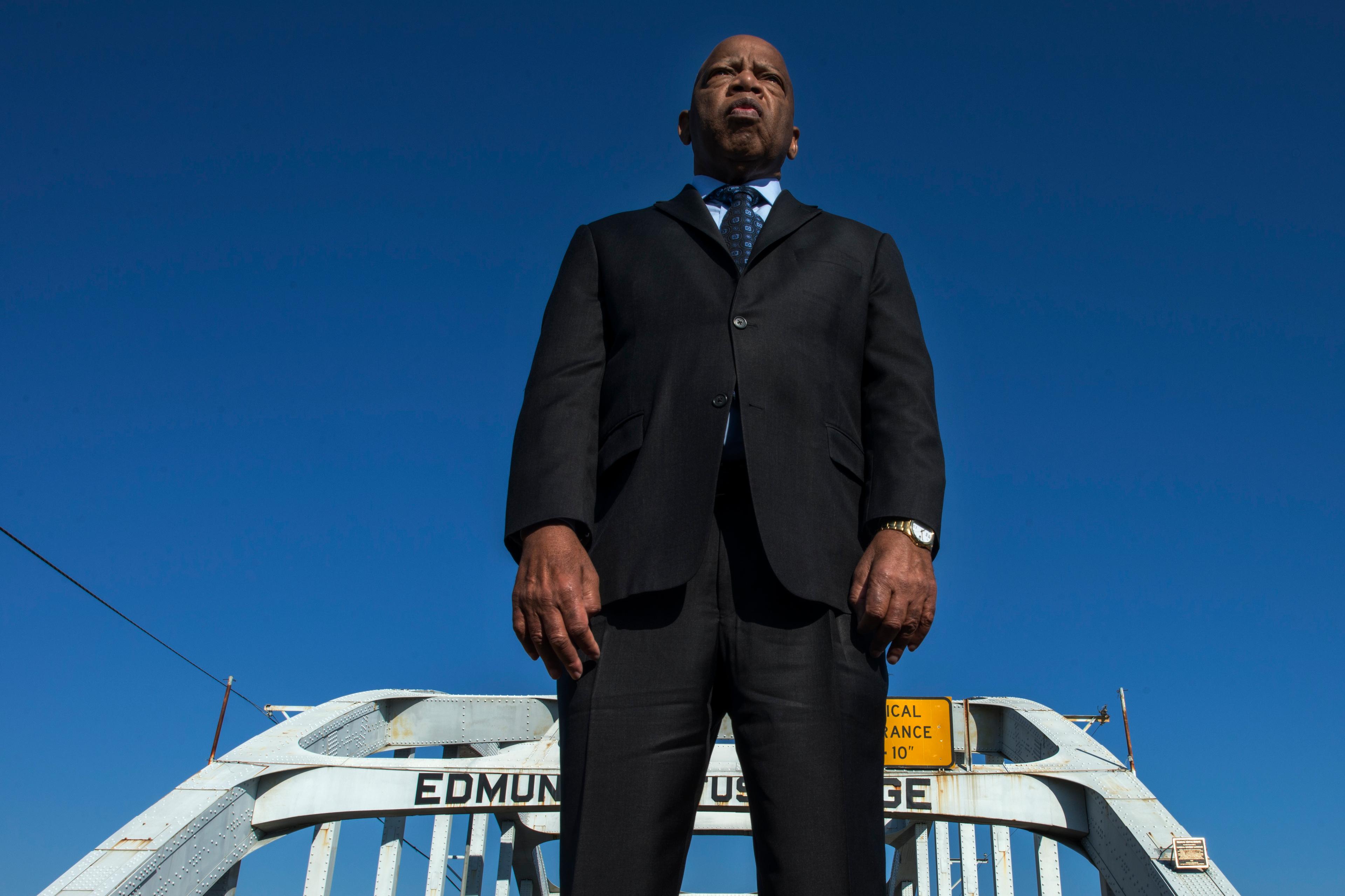Photo of a man in a suit standing on Edmund Pettus Bridge against a clear blue sky.
