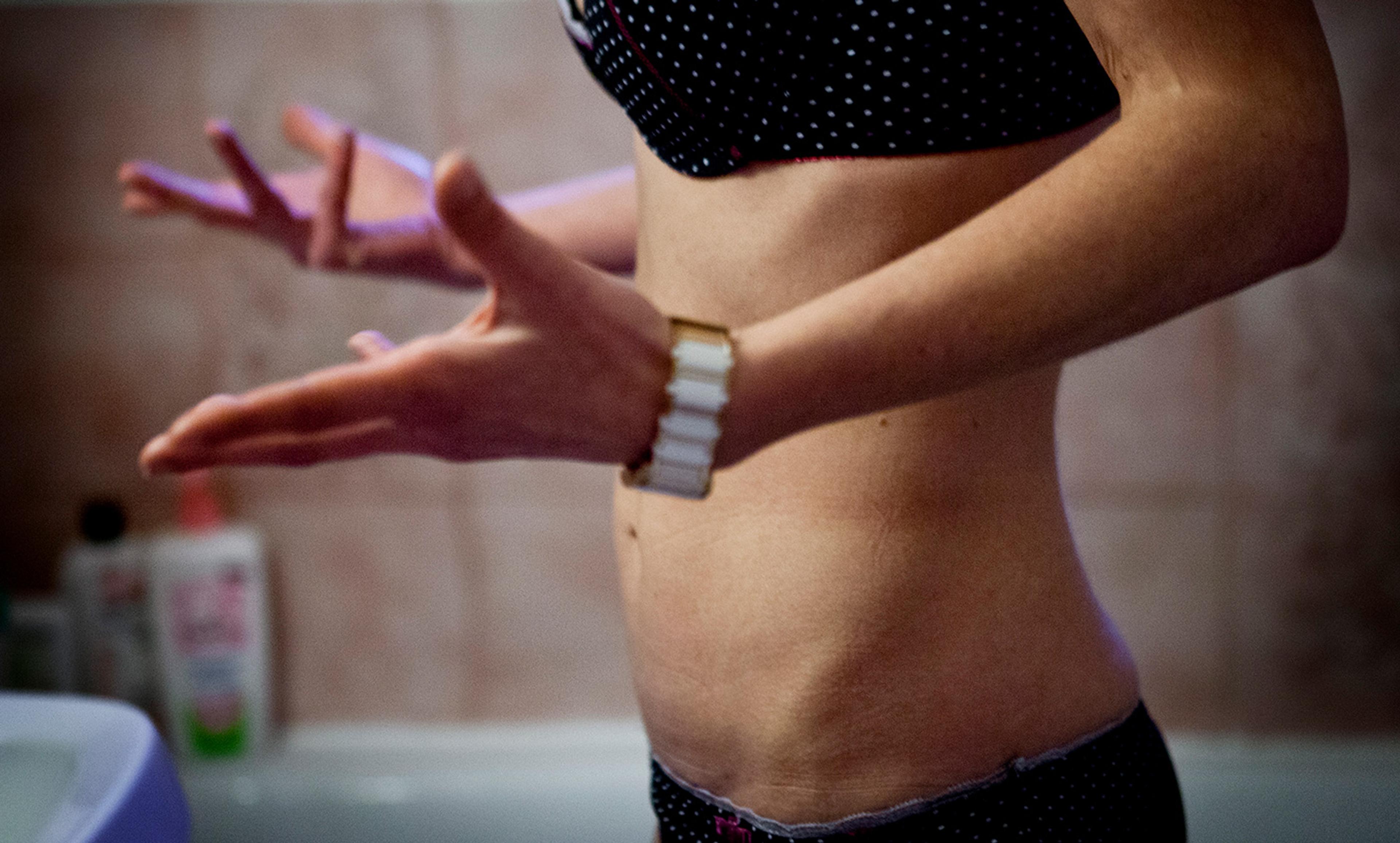 A skinny woman in a polka dot bikini, seen from the torso down, with her hands gesturing near a sink in a bathroom.