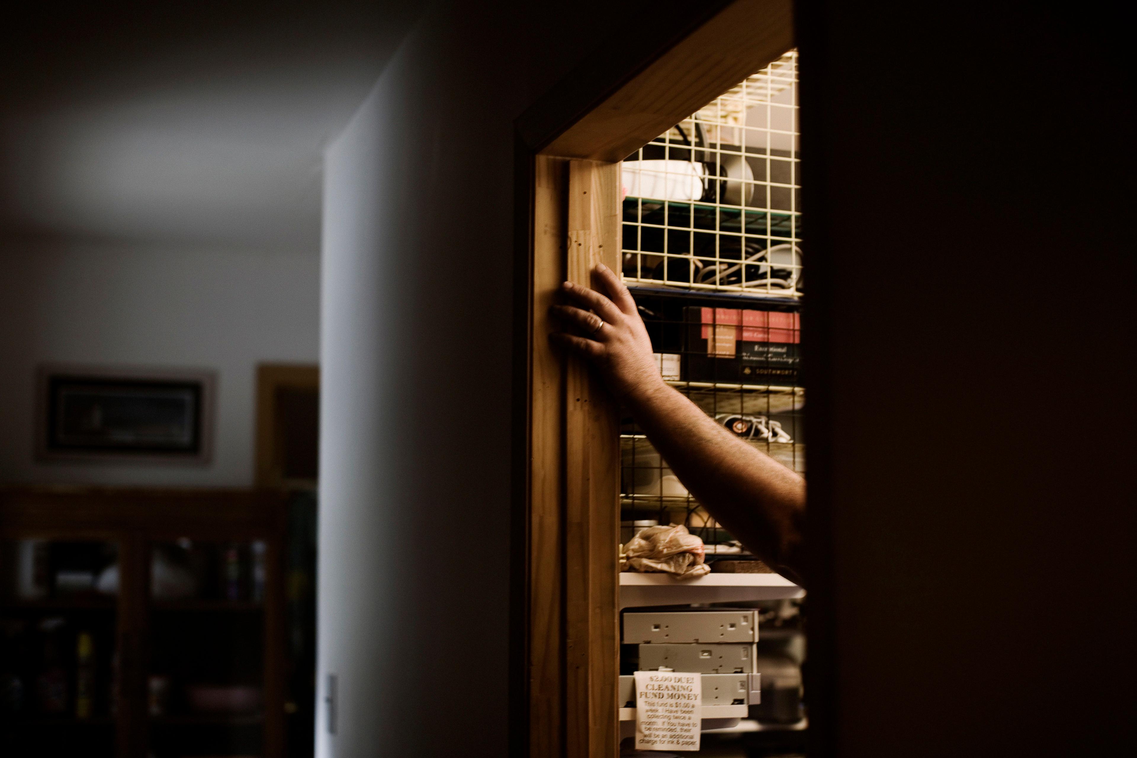 Photo of an arm reaching into a dimly lit cupboard filled with shelves and various items.