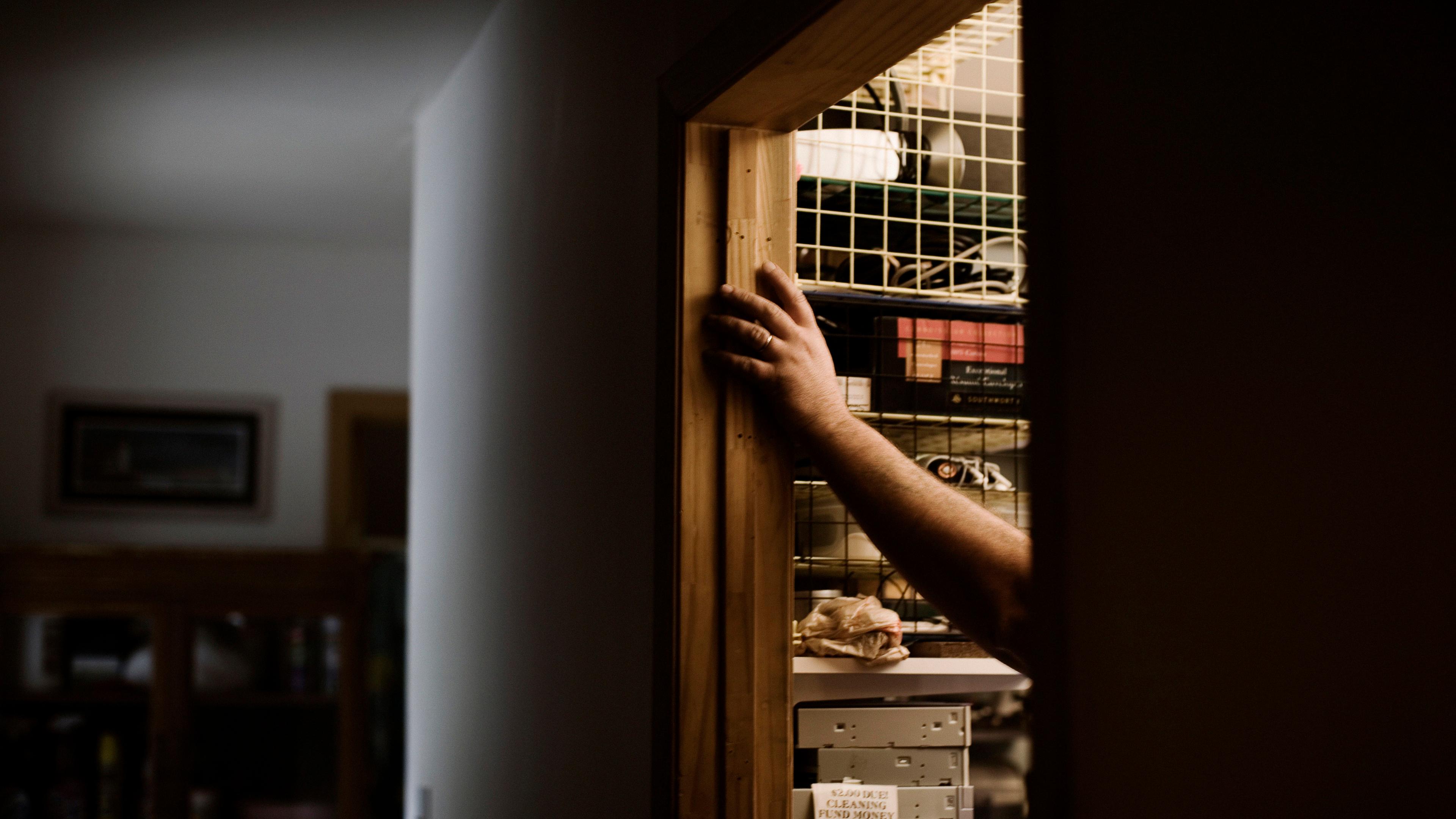 Photo of an arm reaching into a dimly lit cupboard filled with shelves and various items.