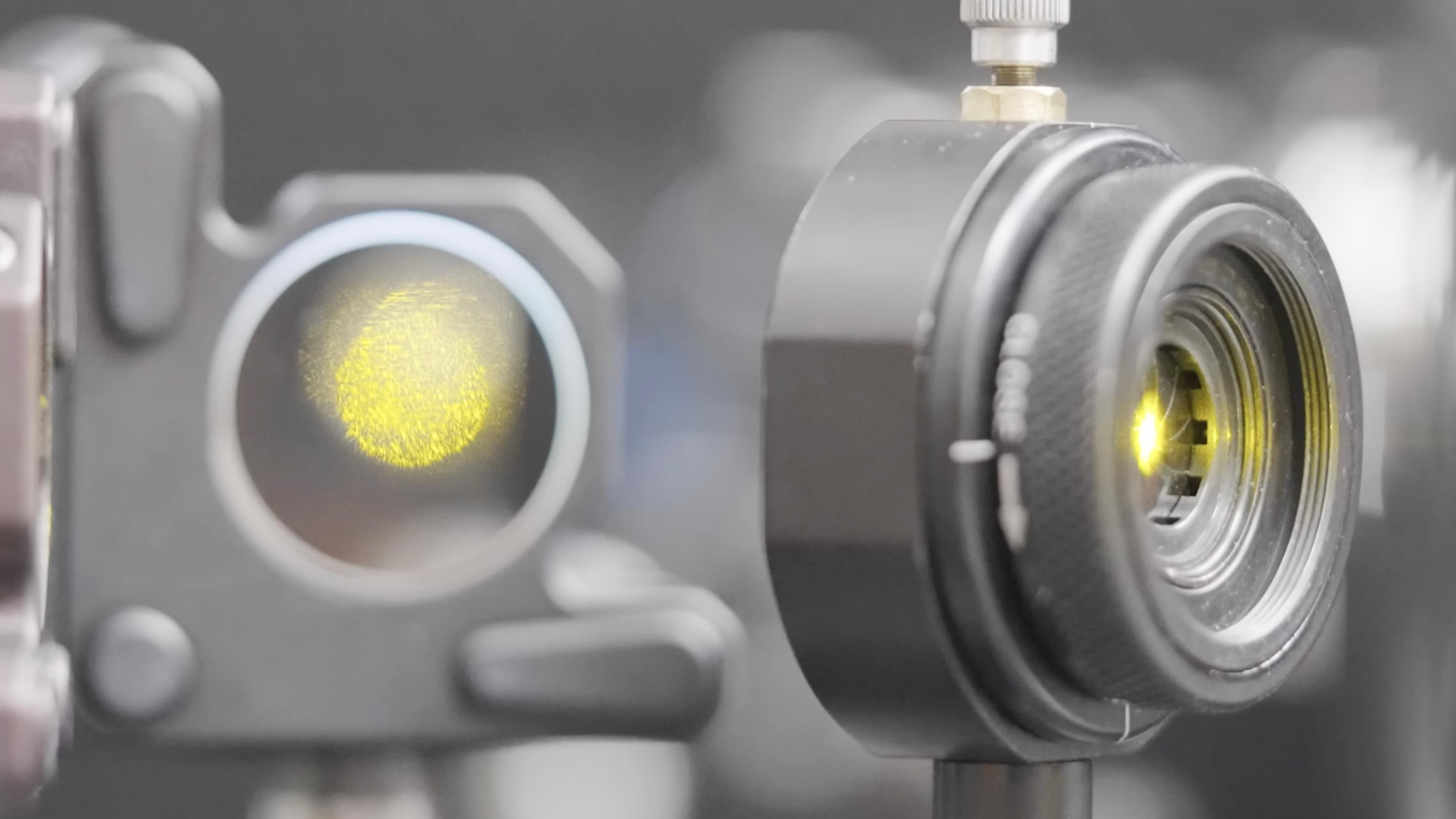 Close-up of two black optical devices with visible yellow light inside the lenses, set against a blurry background.