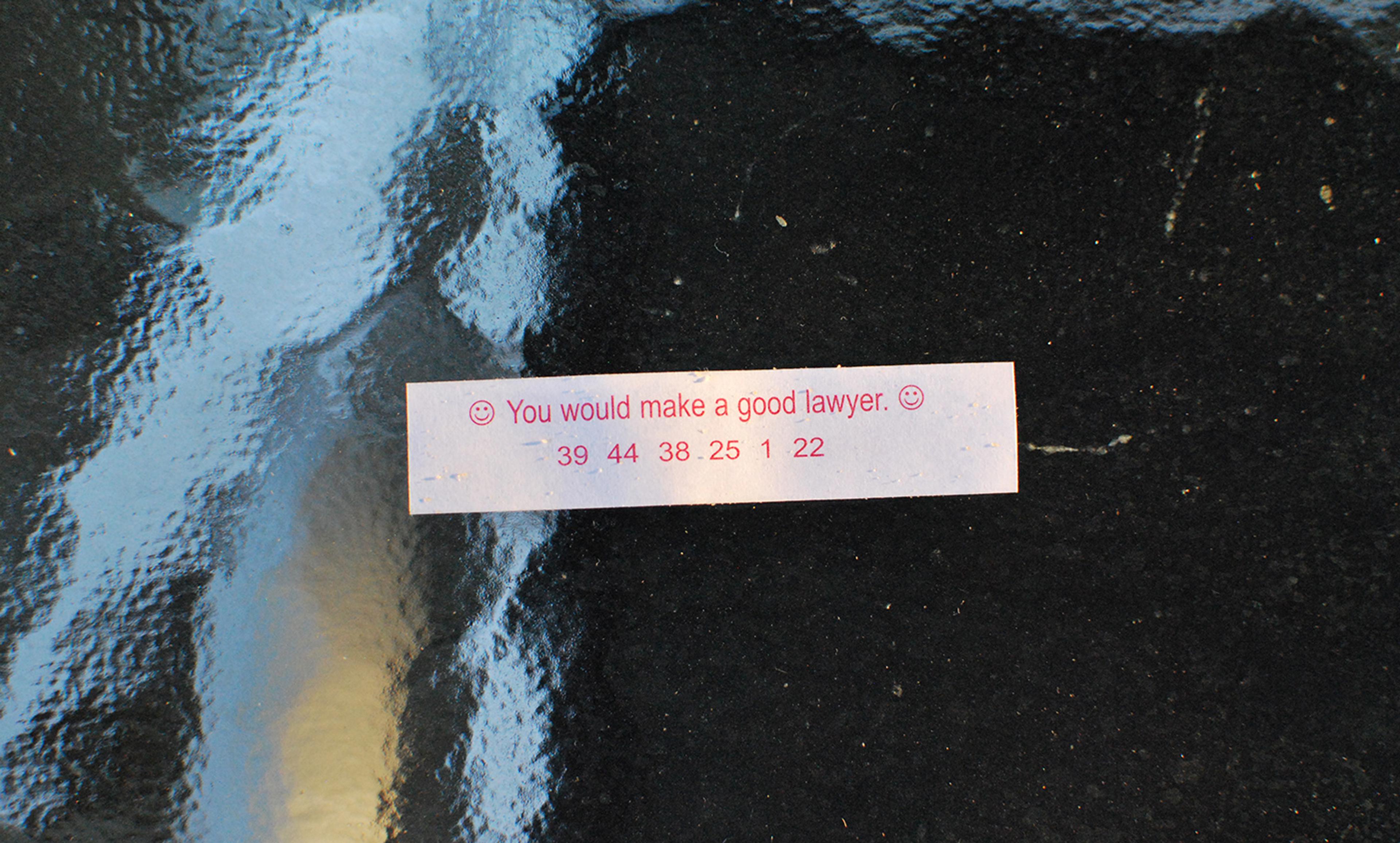 A fortune cookie paper that reads “You would make a good lawyer” with numbers beneath it on a reflective surface.