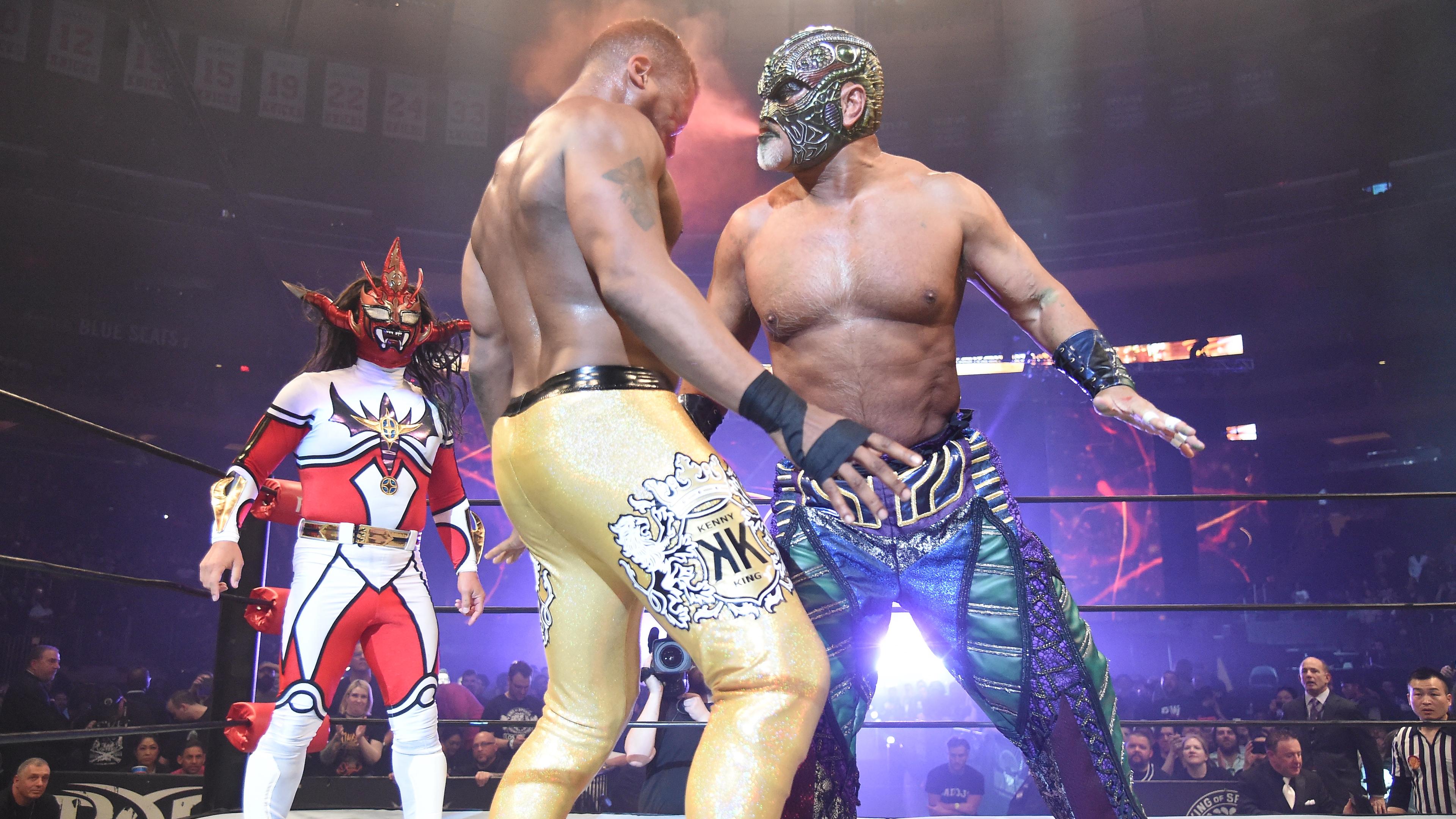 Photo of masked wrestlers in a ring, one in bright red and white, another in gold trousers, with a cheering crowd.