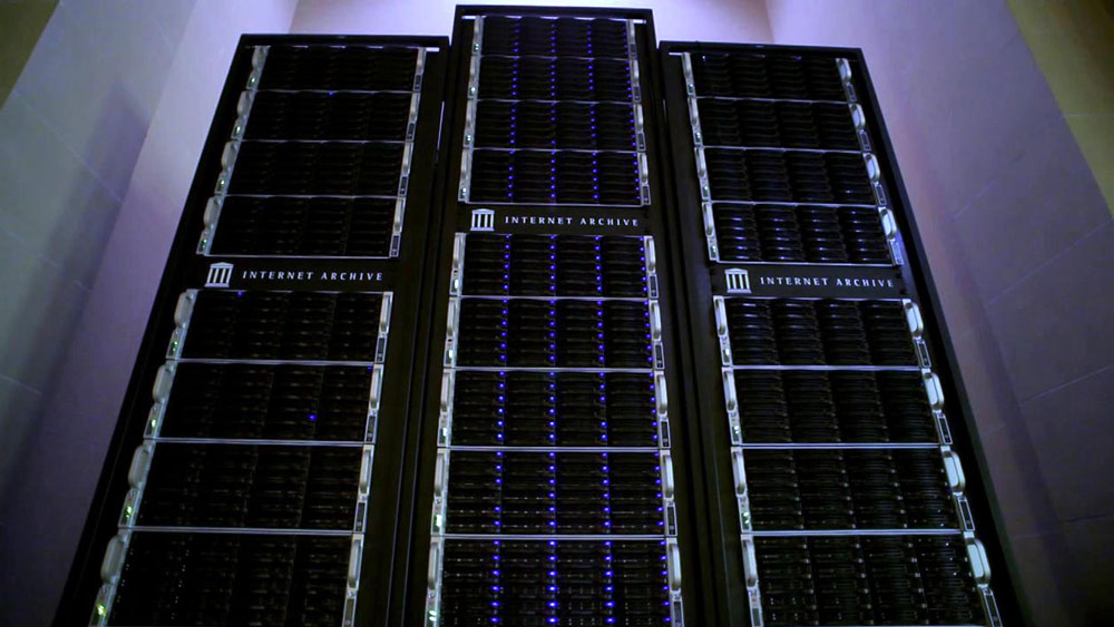 Three large server racks labelled Internet Archive in a well-lit server room with an upward view.