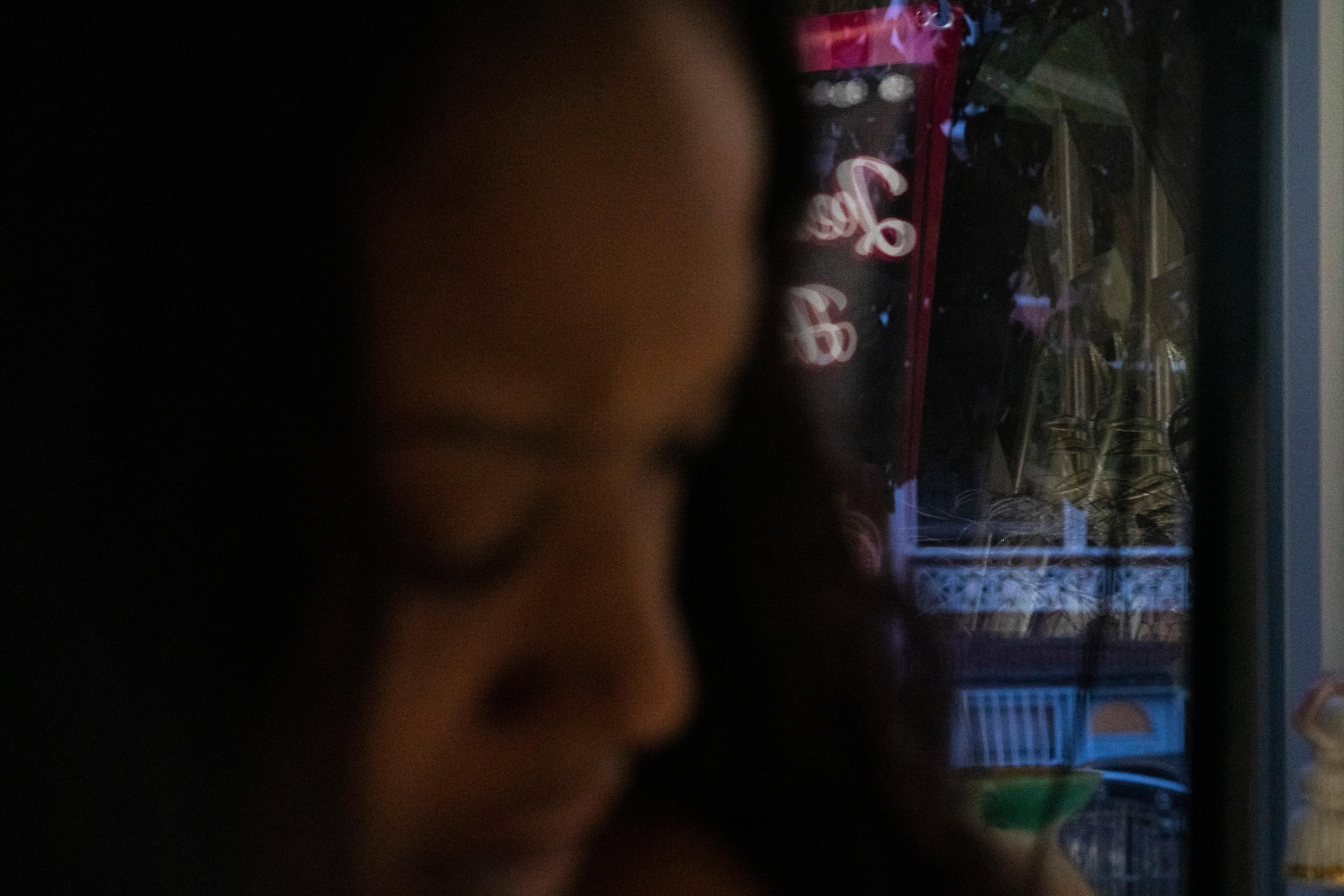 Blurry photo of a person with a colourful neon sign reflected in a window at night.