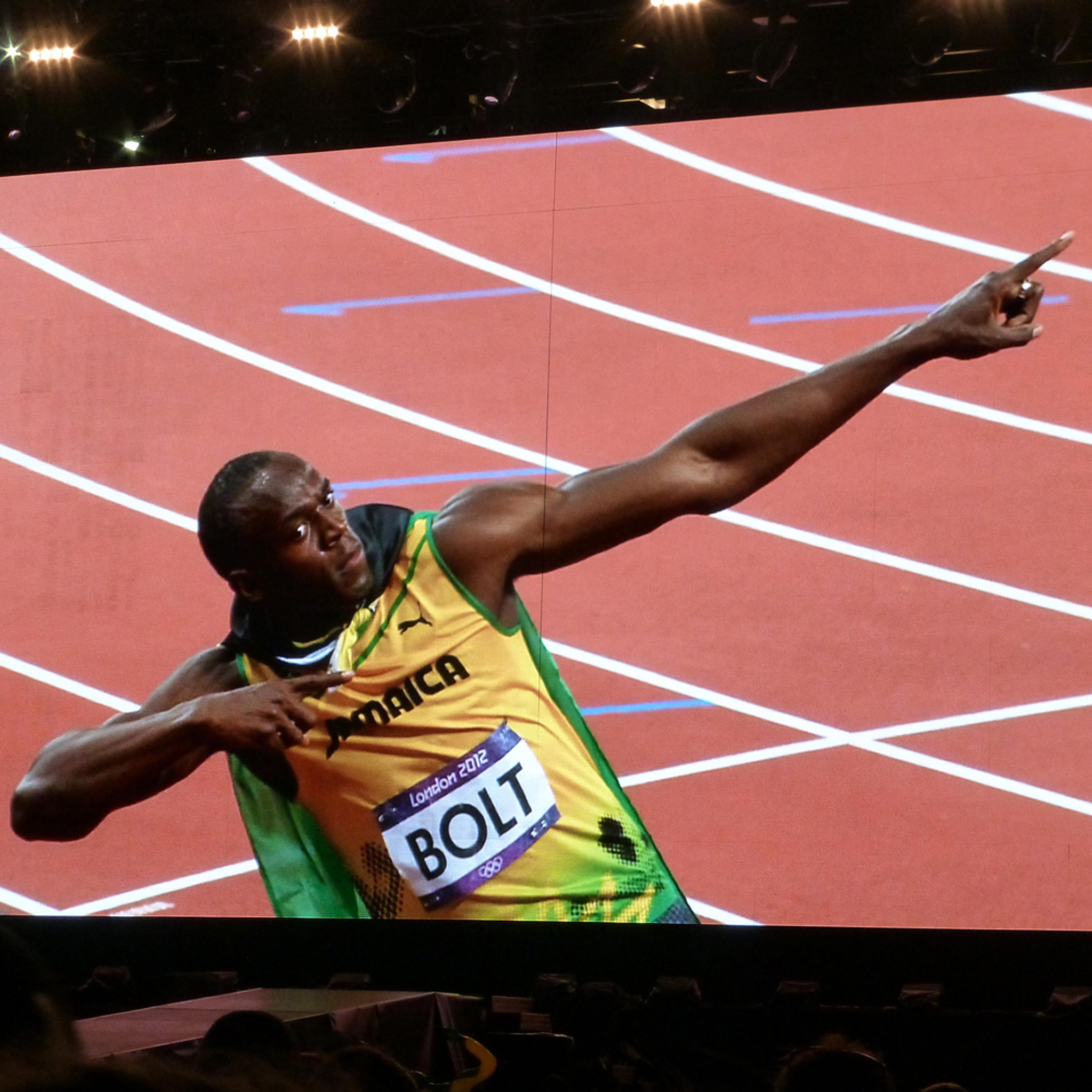 The sprinter Usain Bolt in a yellow and green uniform making a victory pose on a track at the London 2012 Olympics.