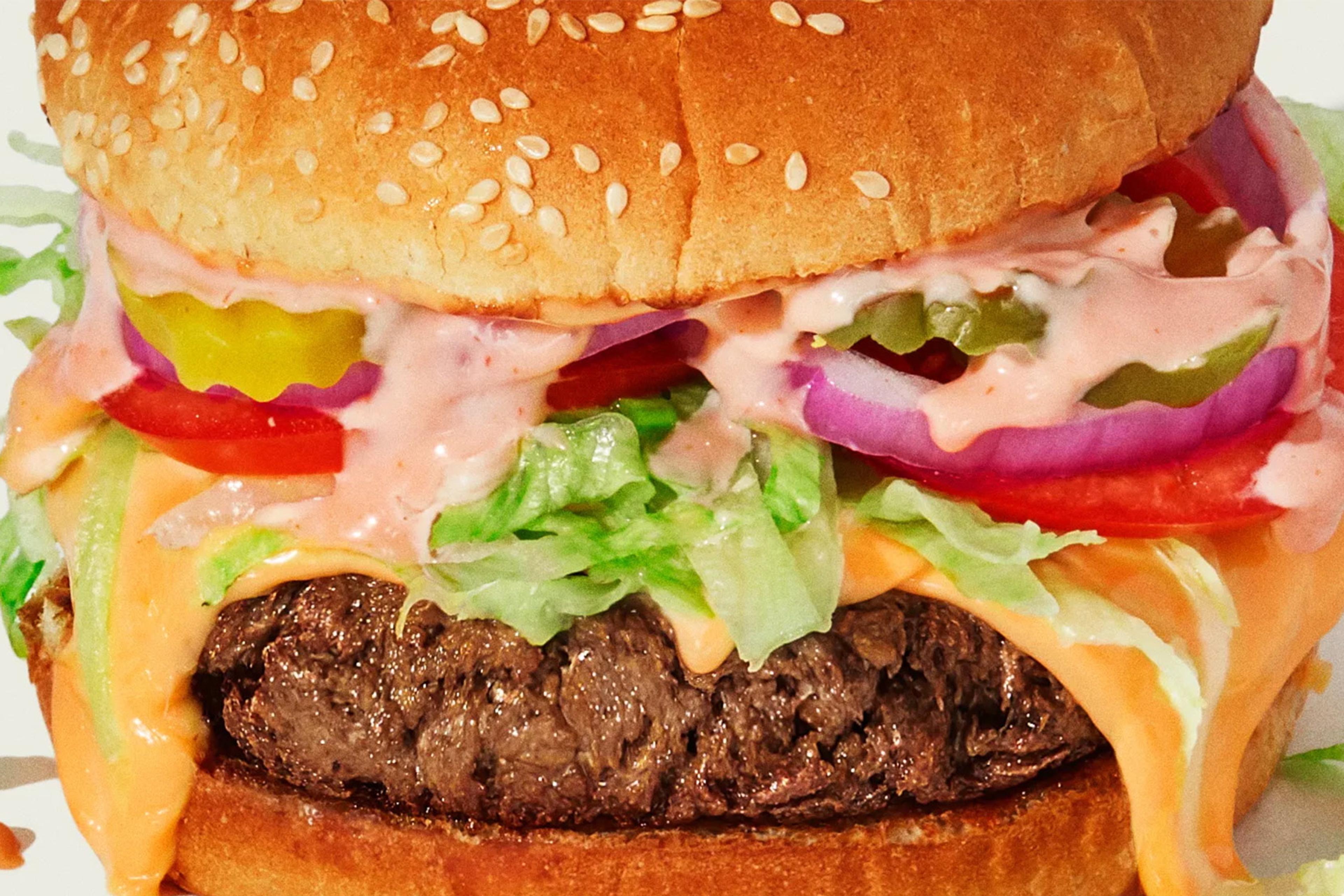 Photo of a close-up hamburger with lettuce, tomato, onion, pickles and sauce on a sesame seed bun.