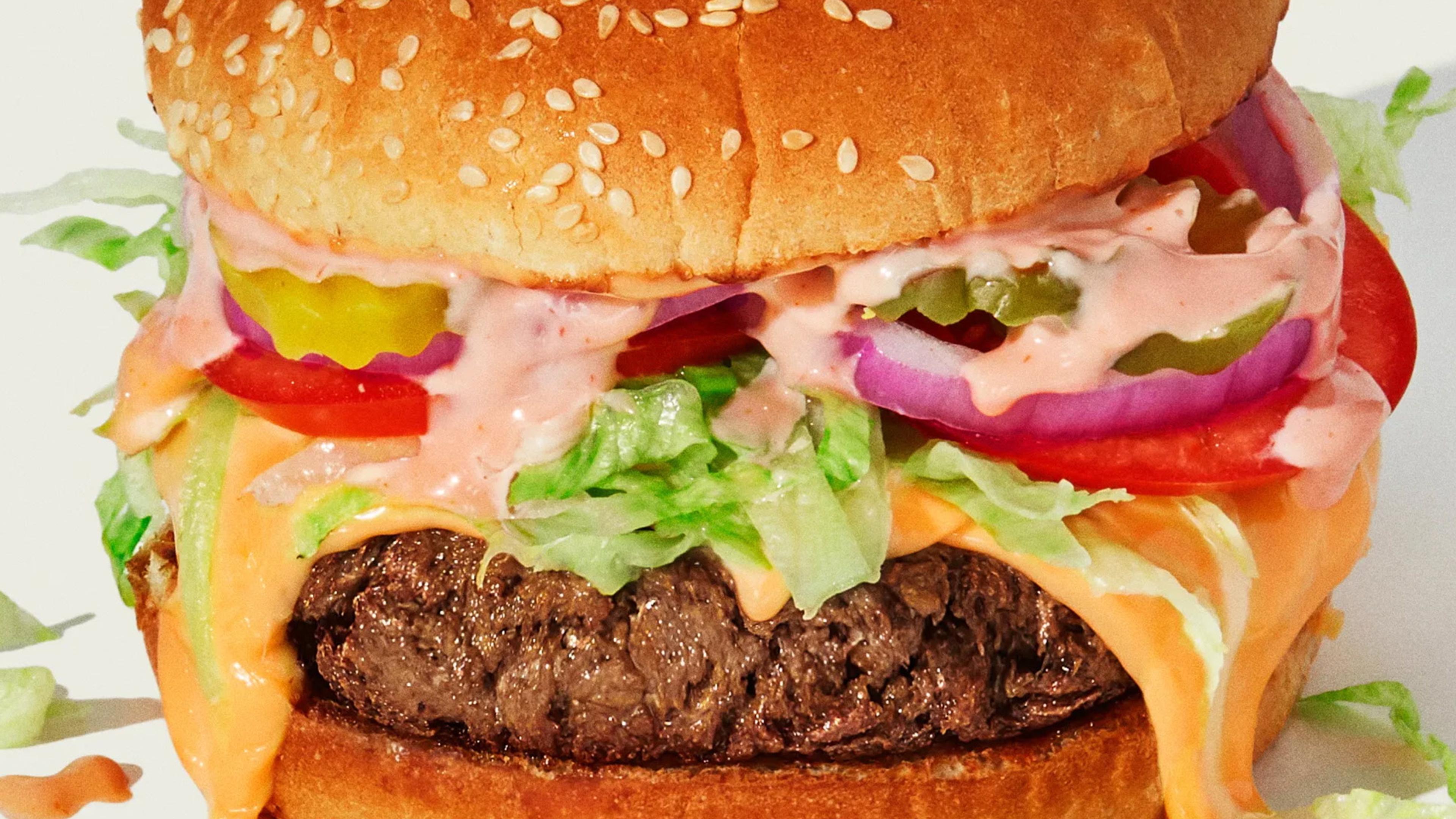 Photo of a close-up hamburger with lettuce, tomato, onion, pickles and sauce on a sesame seed bun.
