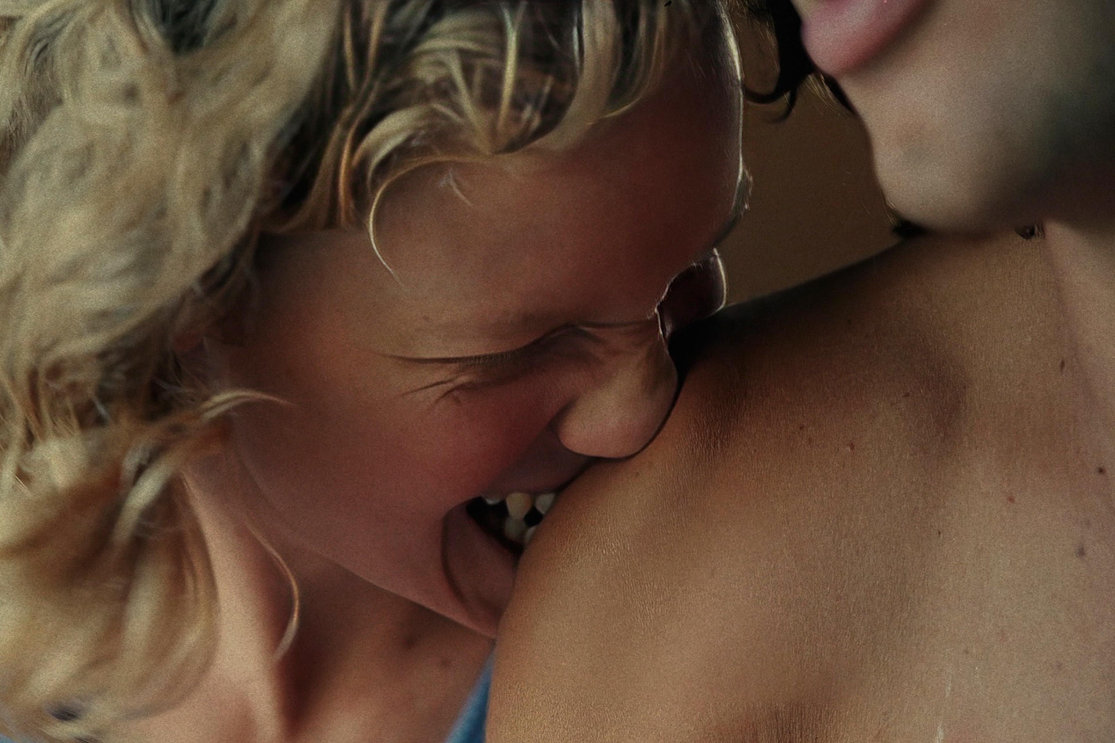 Close-up of a woman with curly hair playfully biting a man’s shoulder while both are smiling.